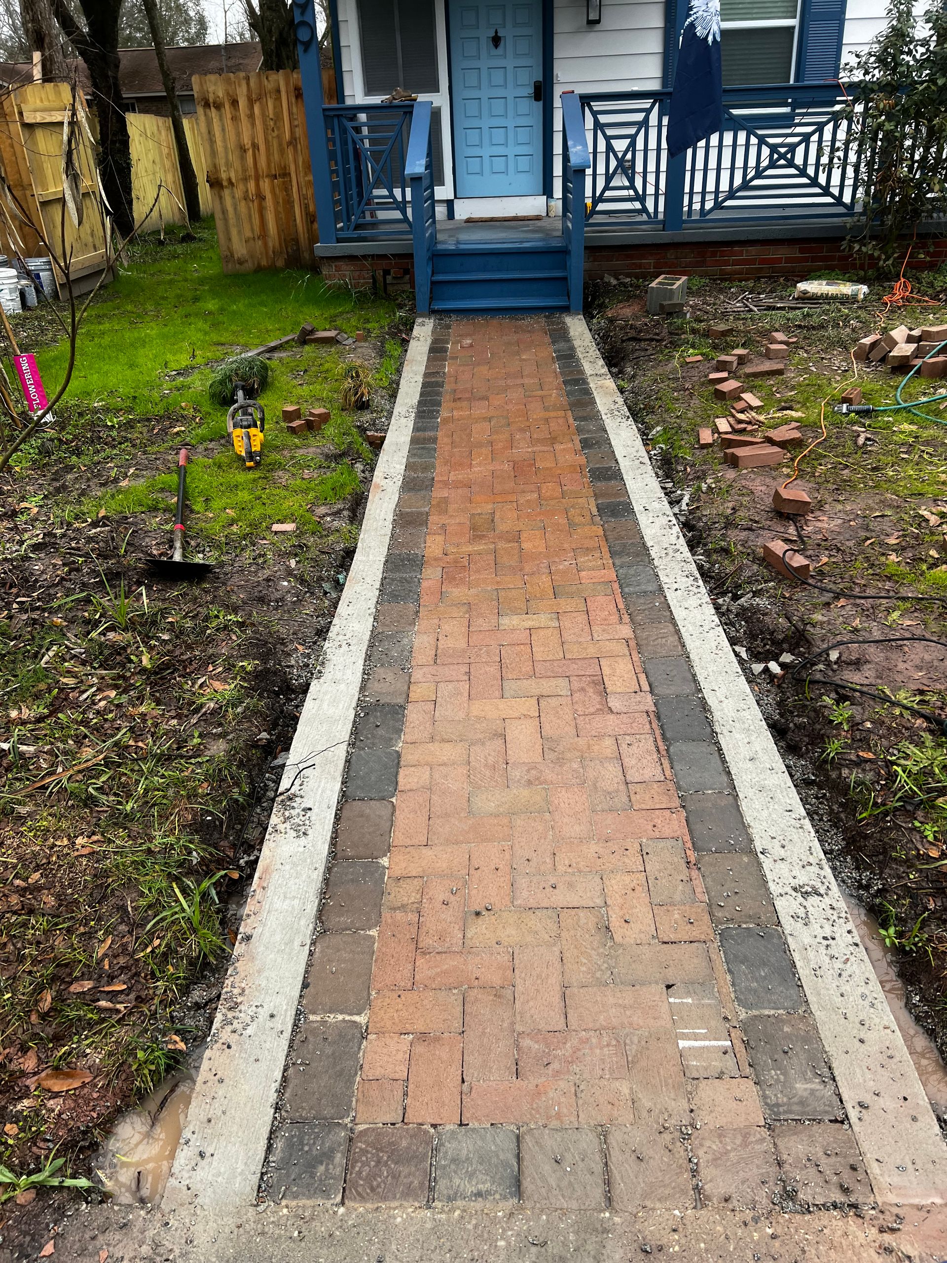 A brick walkway leading to a house with a blue porch.