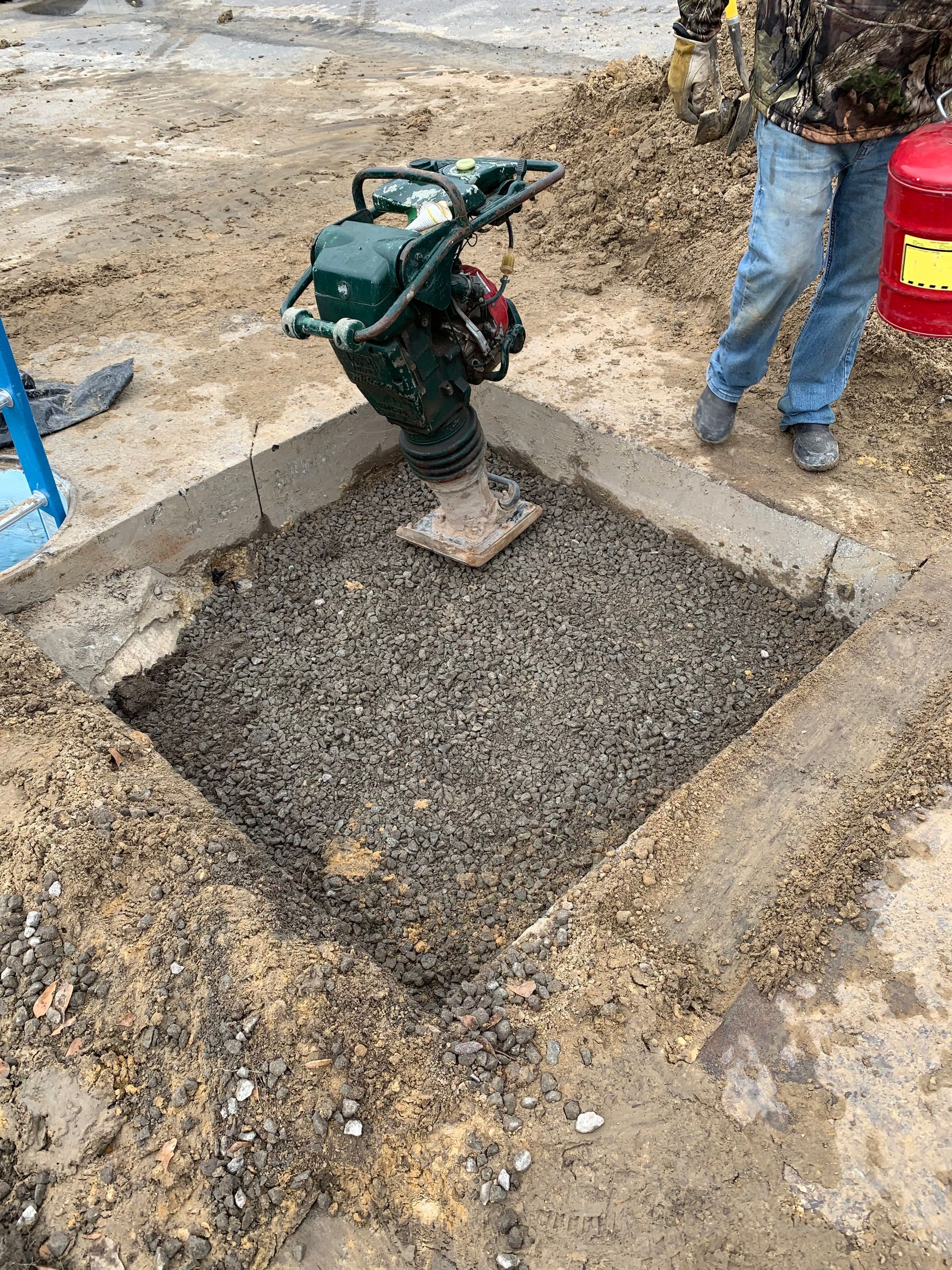 A man is standing next to a machine that is sitting on top of a pile of dirt.