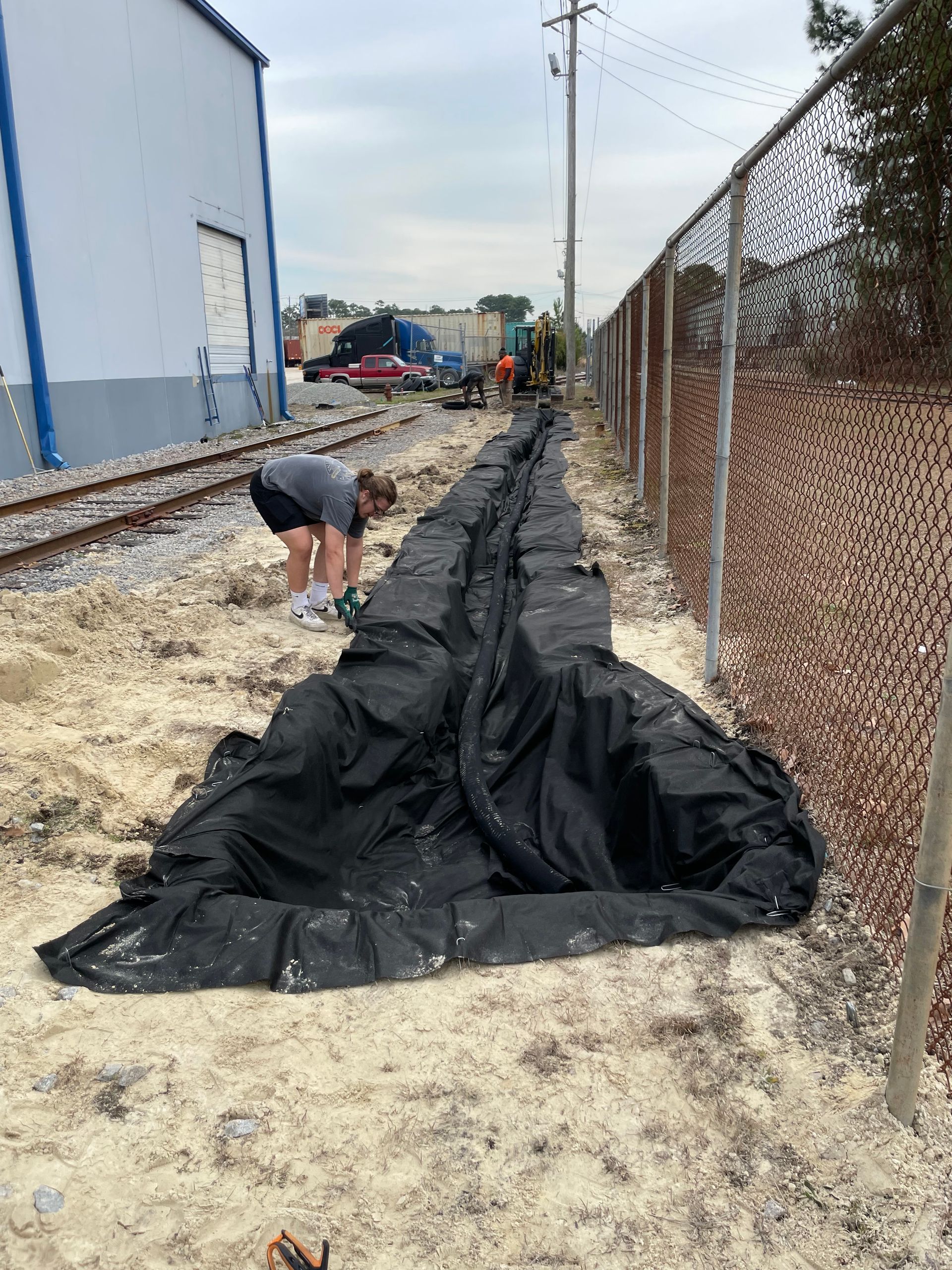 A woman is digging a hole in the ground next to a fence.