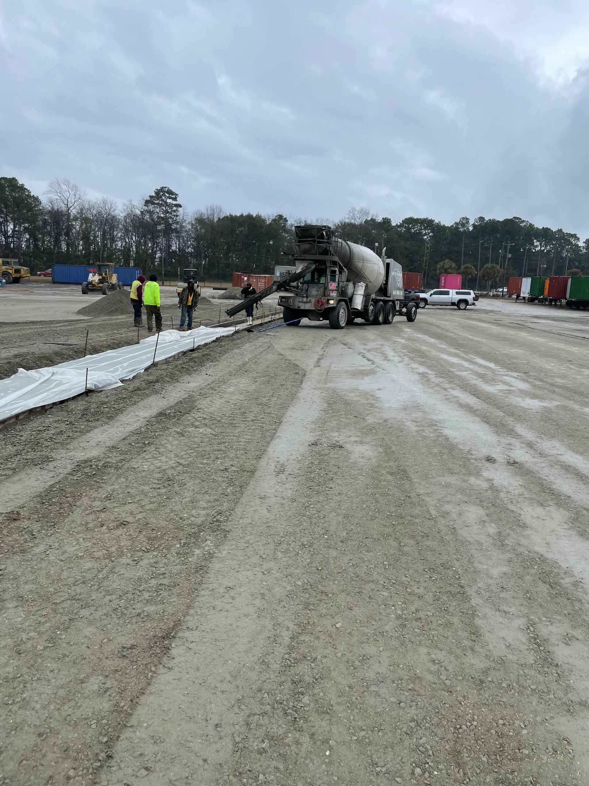 A concrete mixer is pouring concrete into a dirt field.