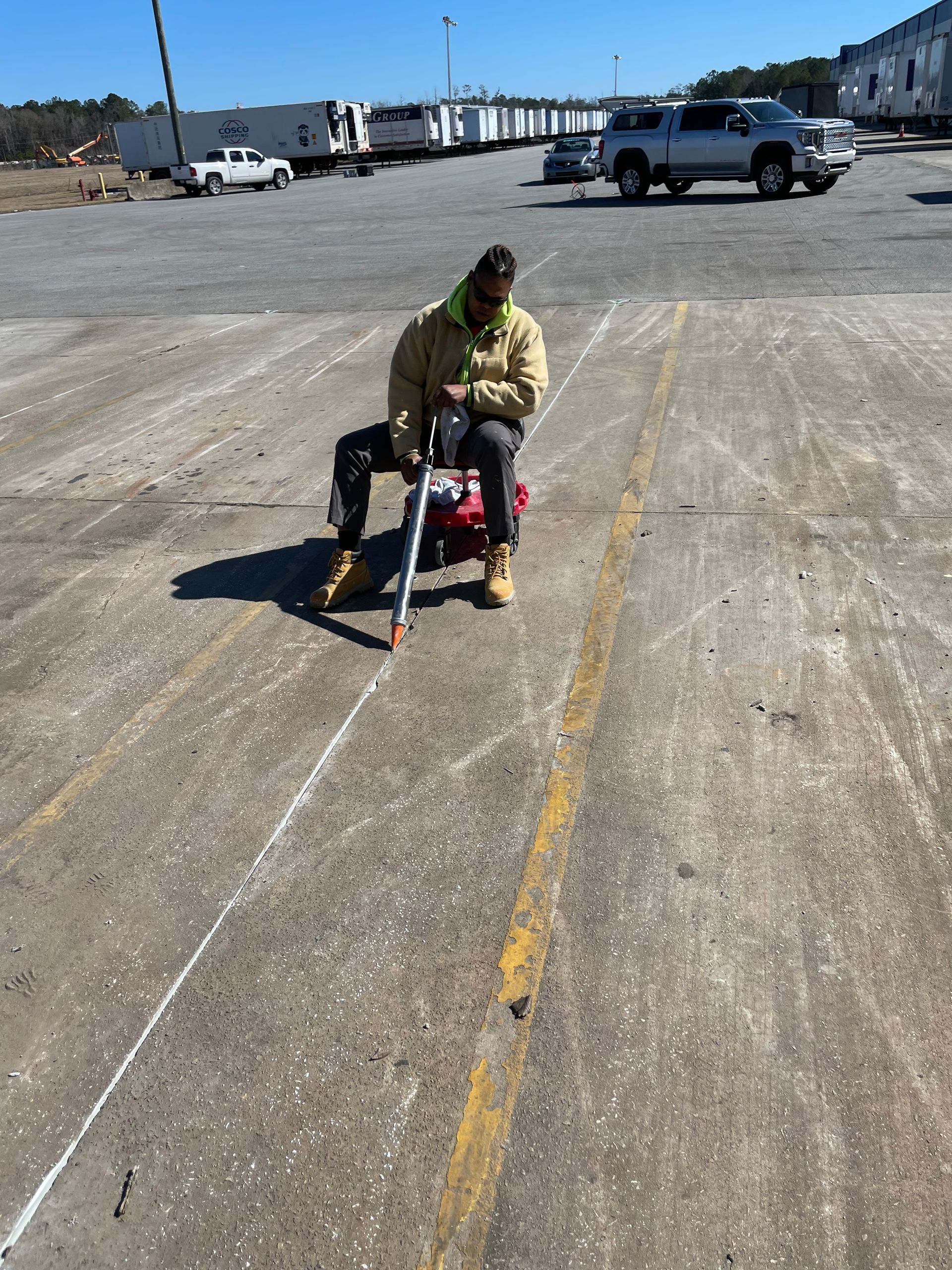 A man is kneeling down in a parking lot using a tool.