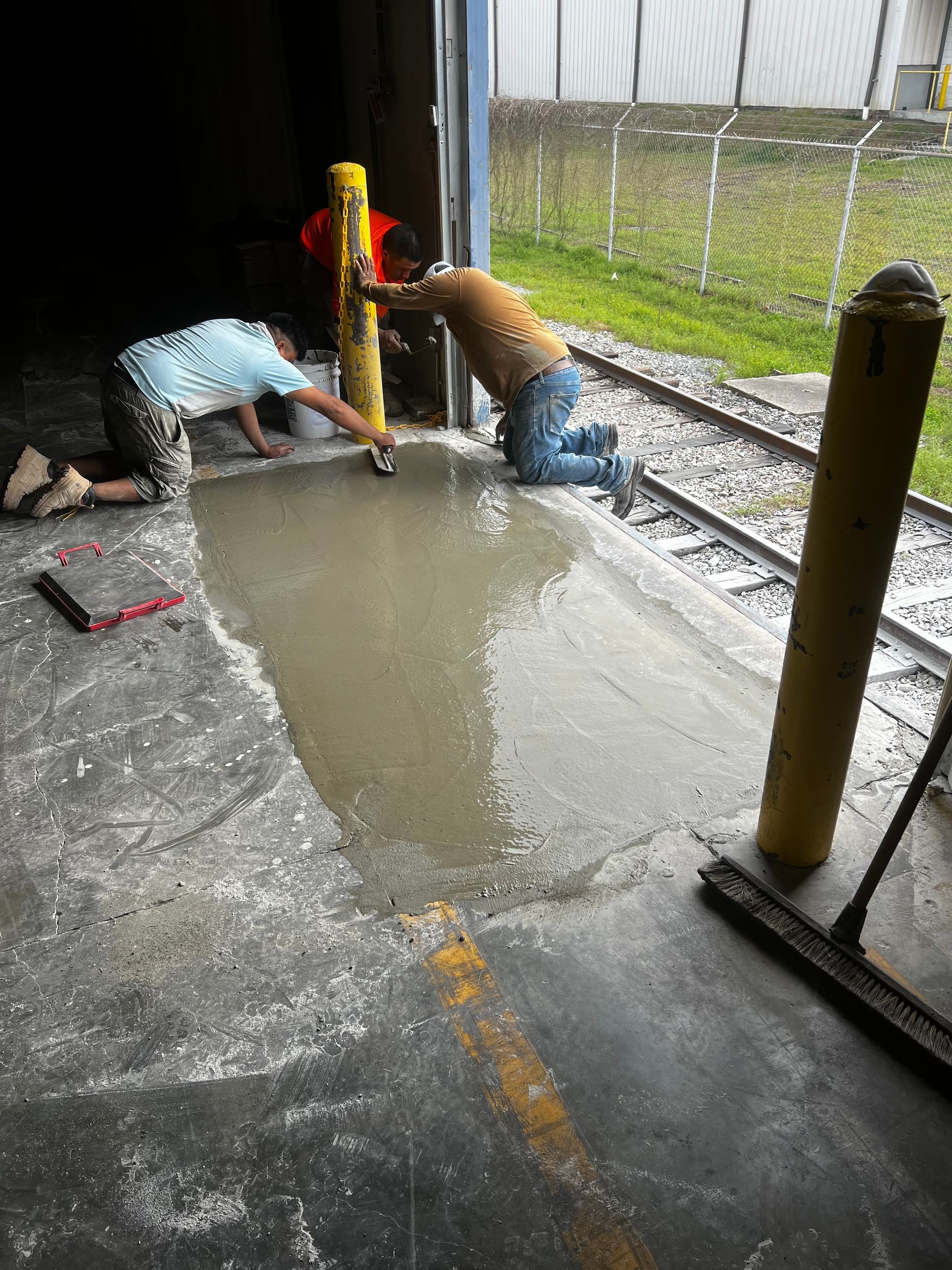 Two men are working on a concrete floor next to train tracks