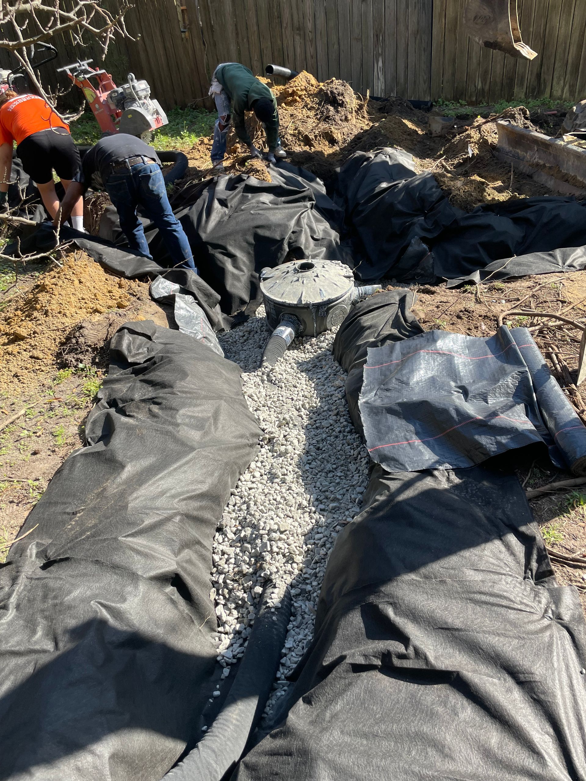 A group of people are working on a drainage system in a backyard.