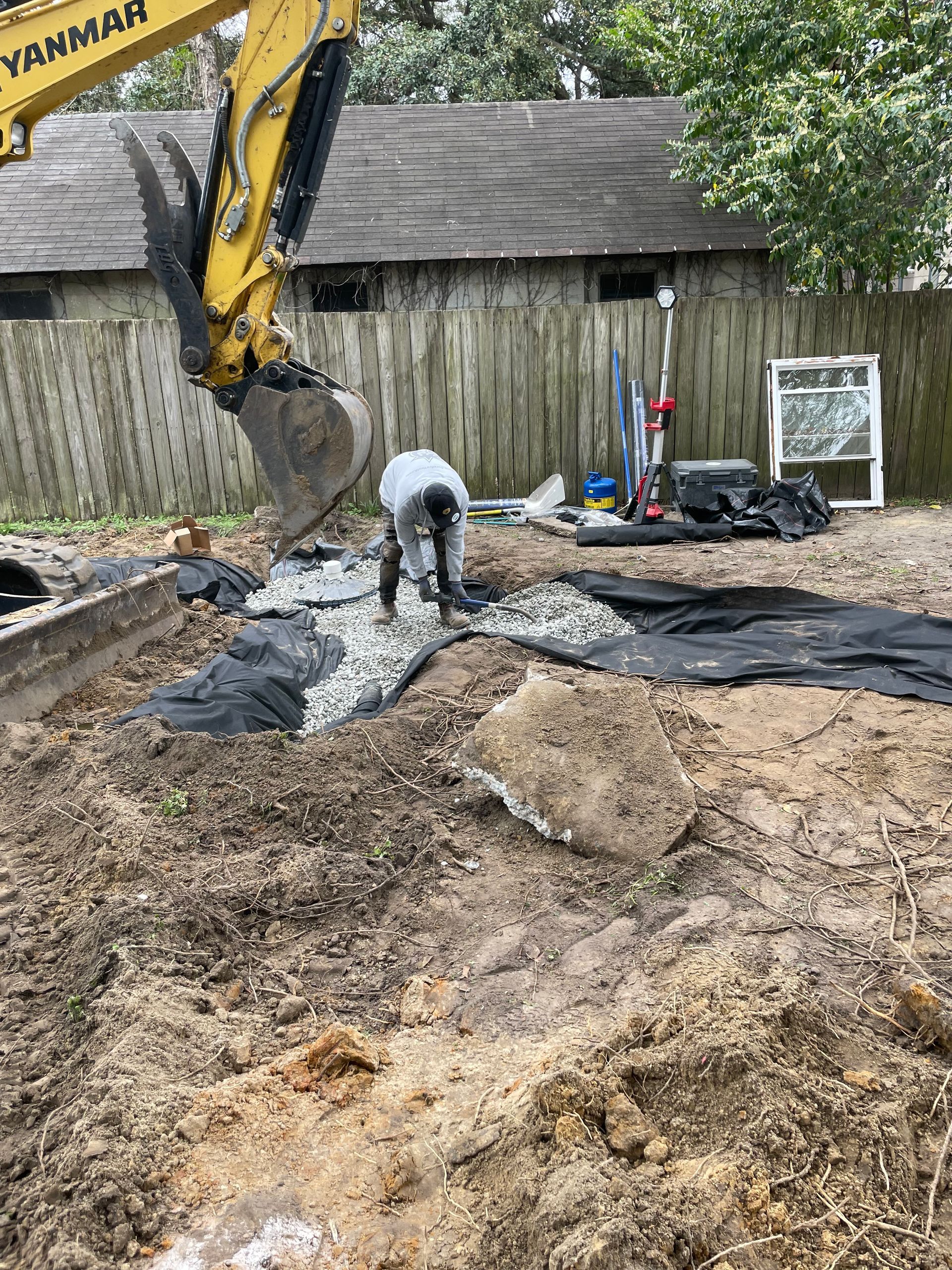 A man is standing in the dirt in front of a yellow excavator.