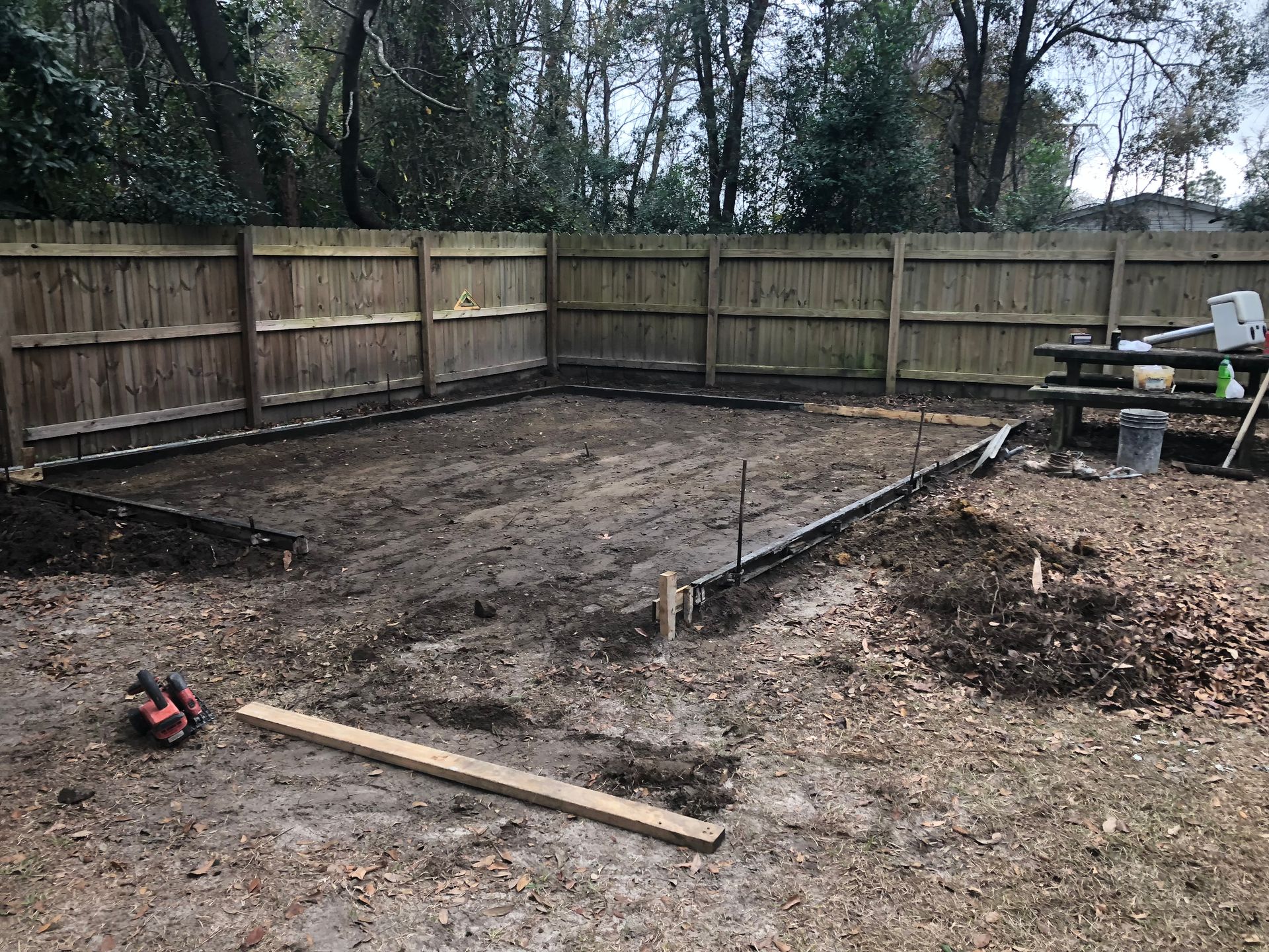 A dirt yard with a wooden fence and a picnic table in the background.