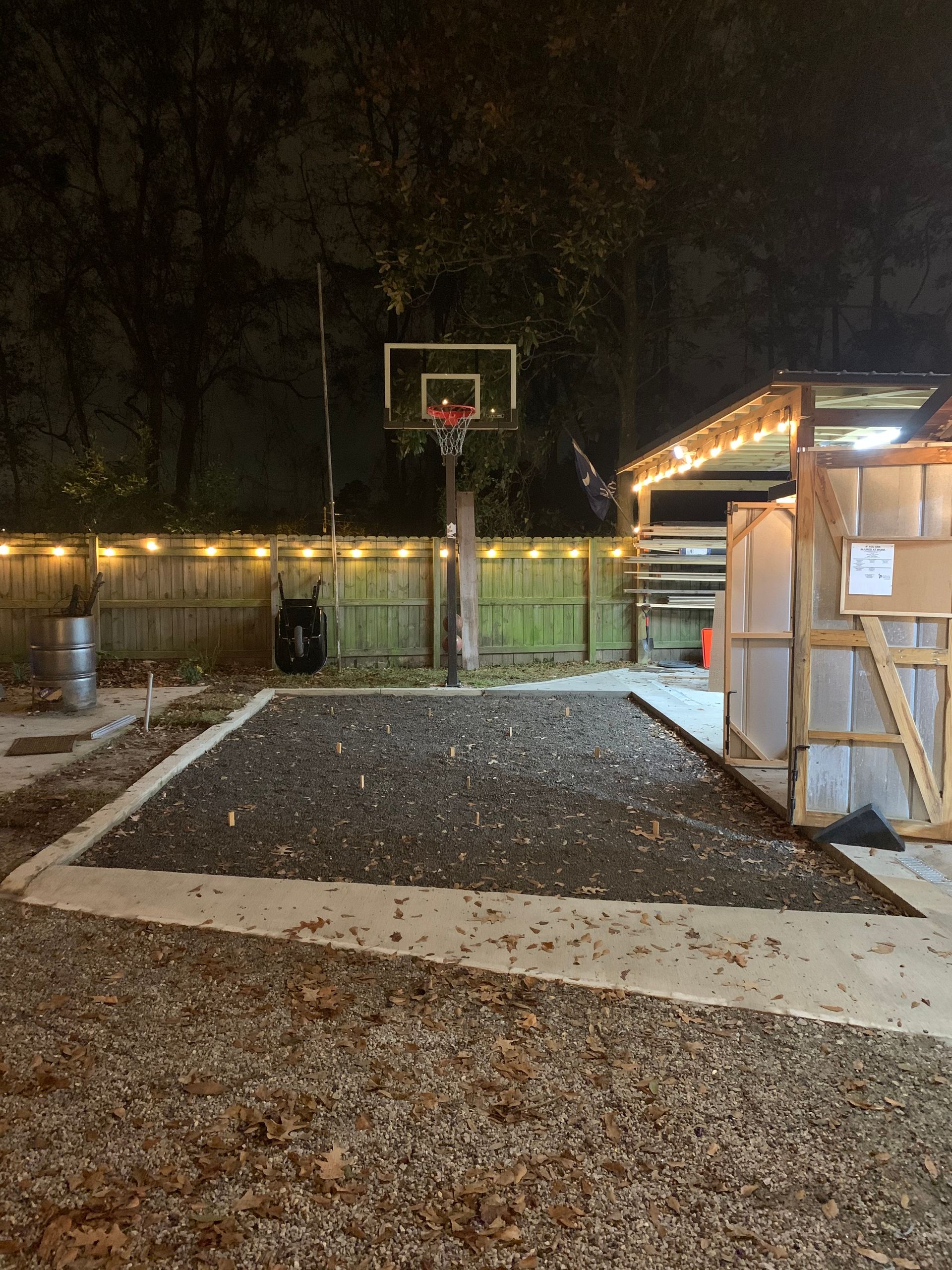 A basketball hoop is in the backyard at night.