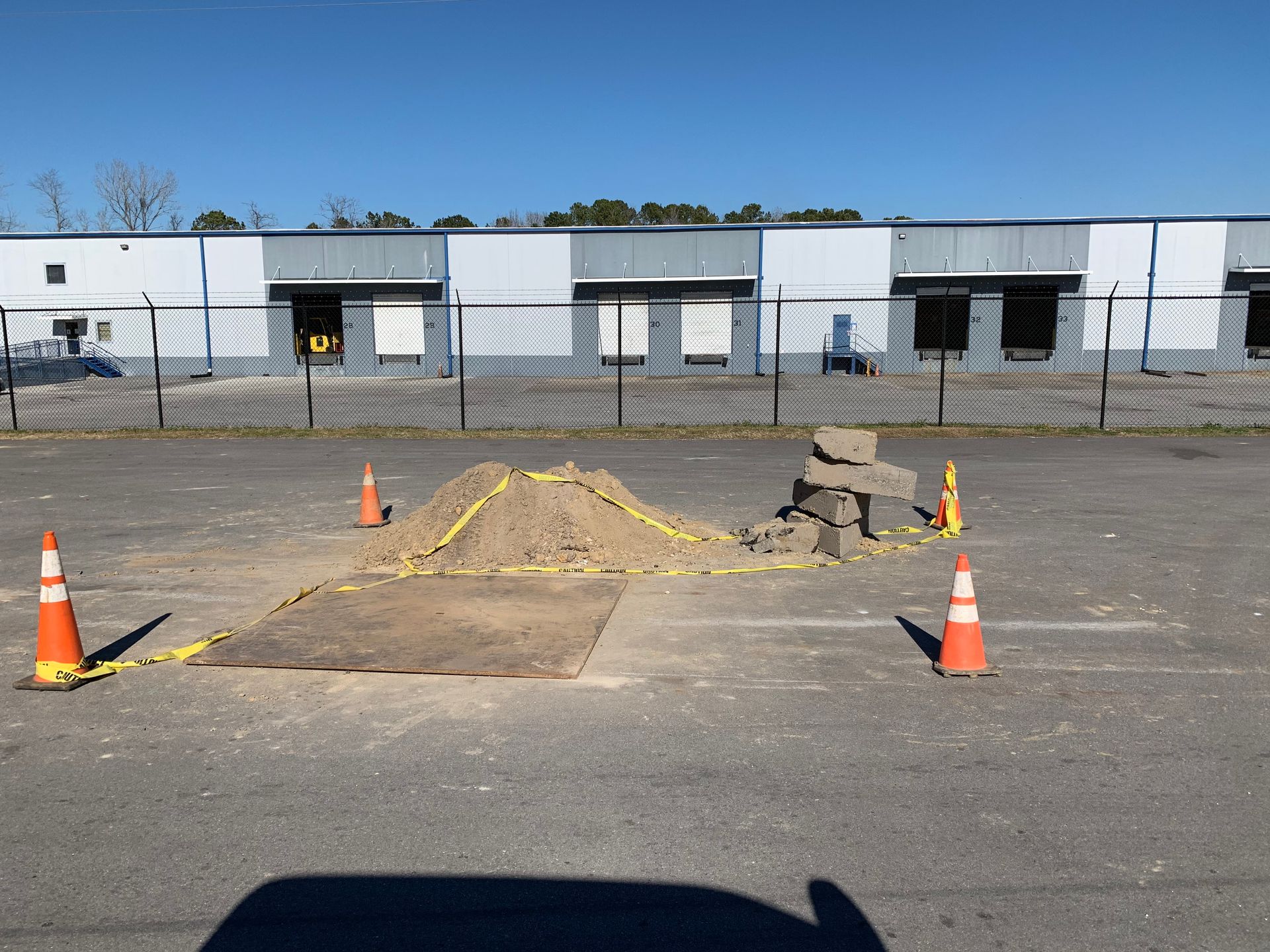 A large pile of dirt is sitting in a parking lot surrounded by traffic cones