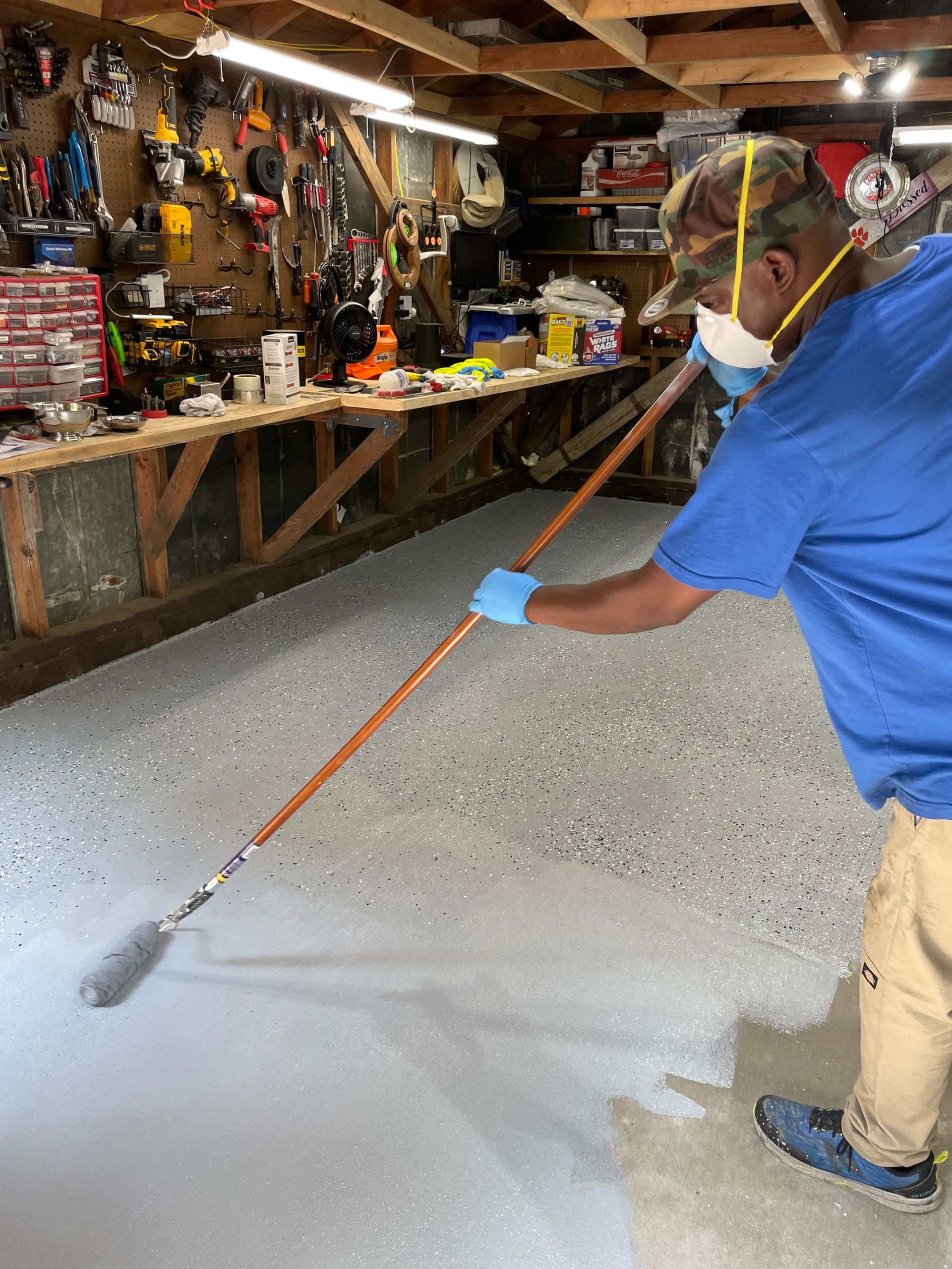 A man wearing a mask and gloves is painting a garage floor.