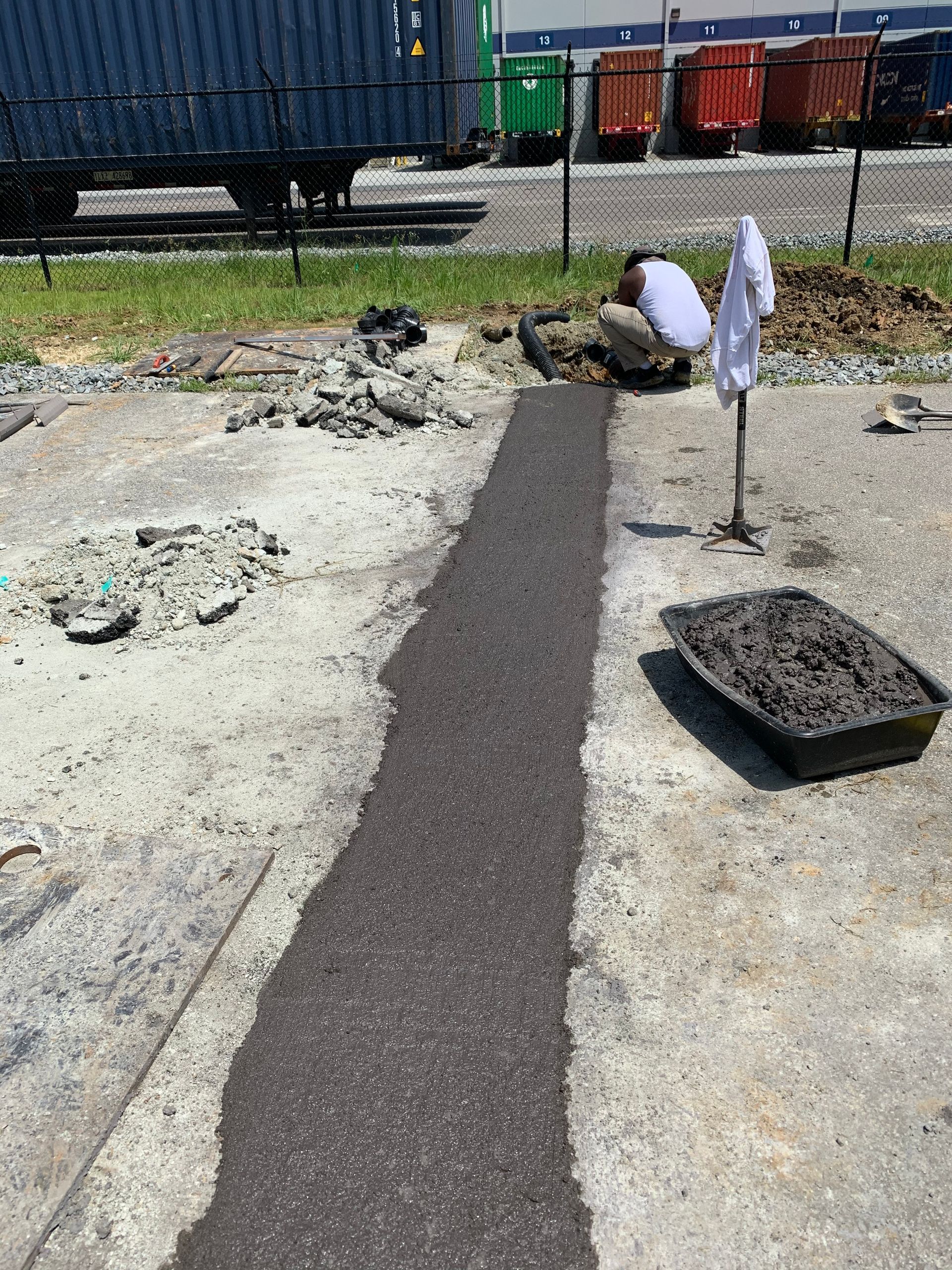 A man is working on a sidewalk in a parking lot.