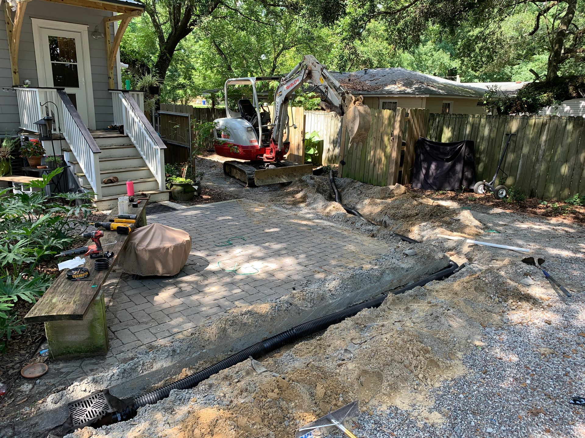 A small excavator is digging a hole in the dirt in front of a house.