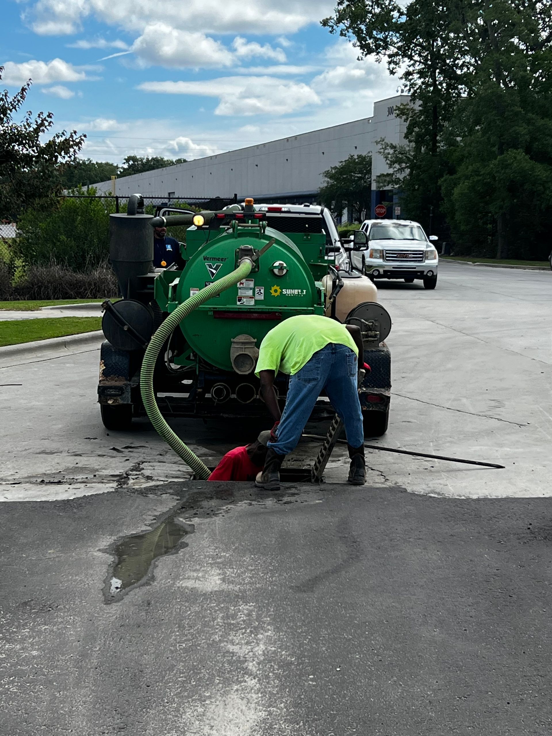 A man is standing next to a green vacuum truck in a parking lot.