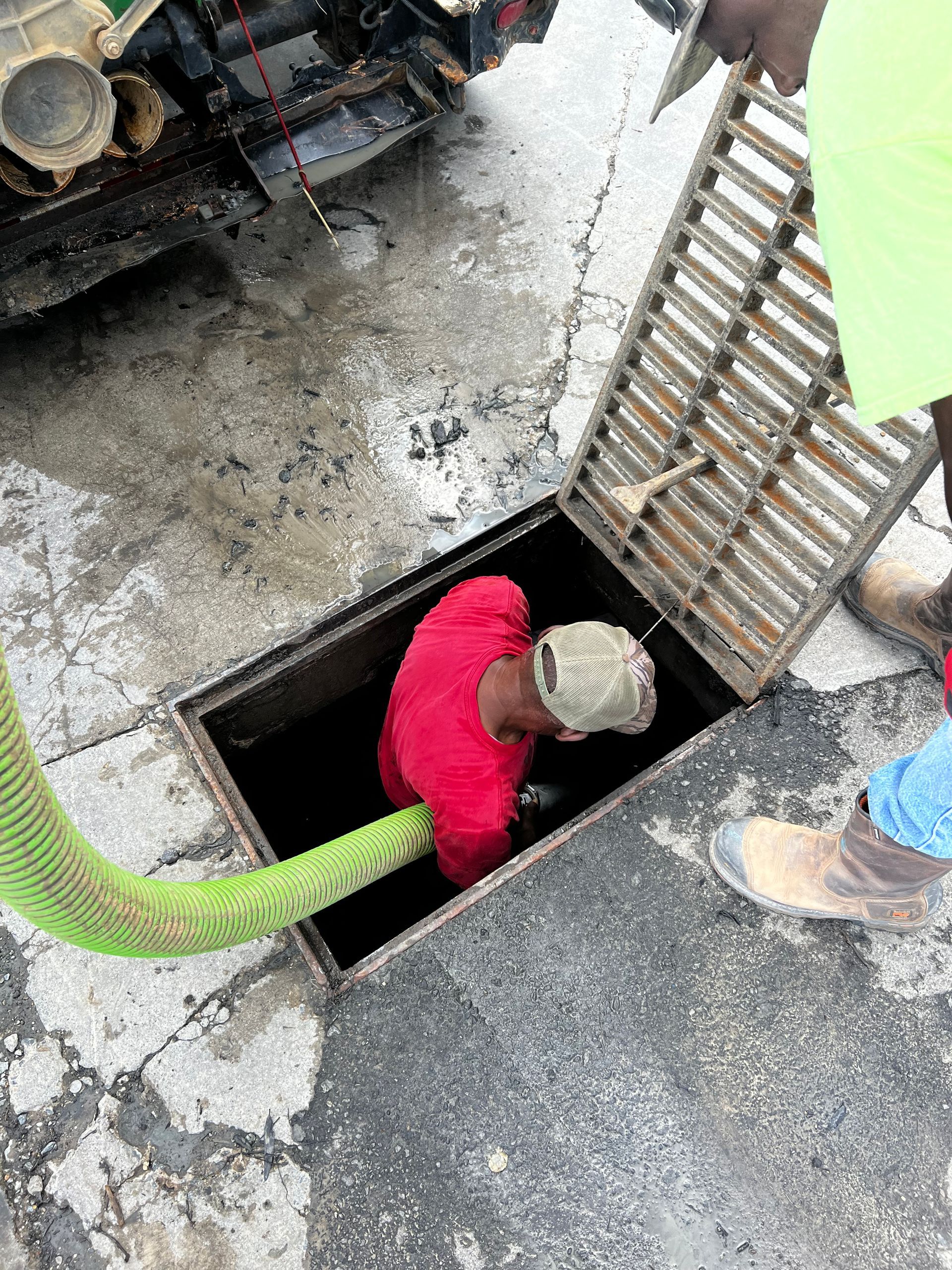 A man is crawling into a manhole cover with a green hose.