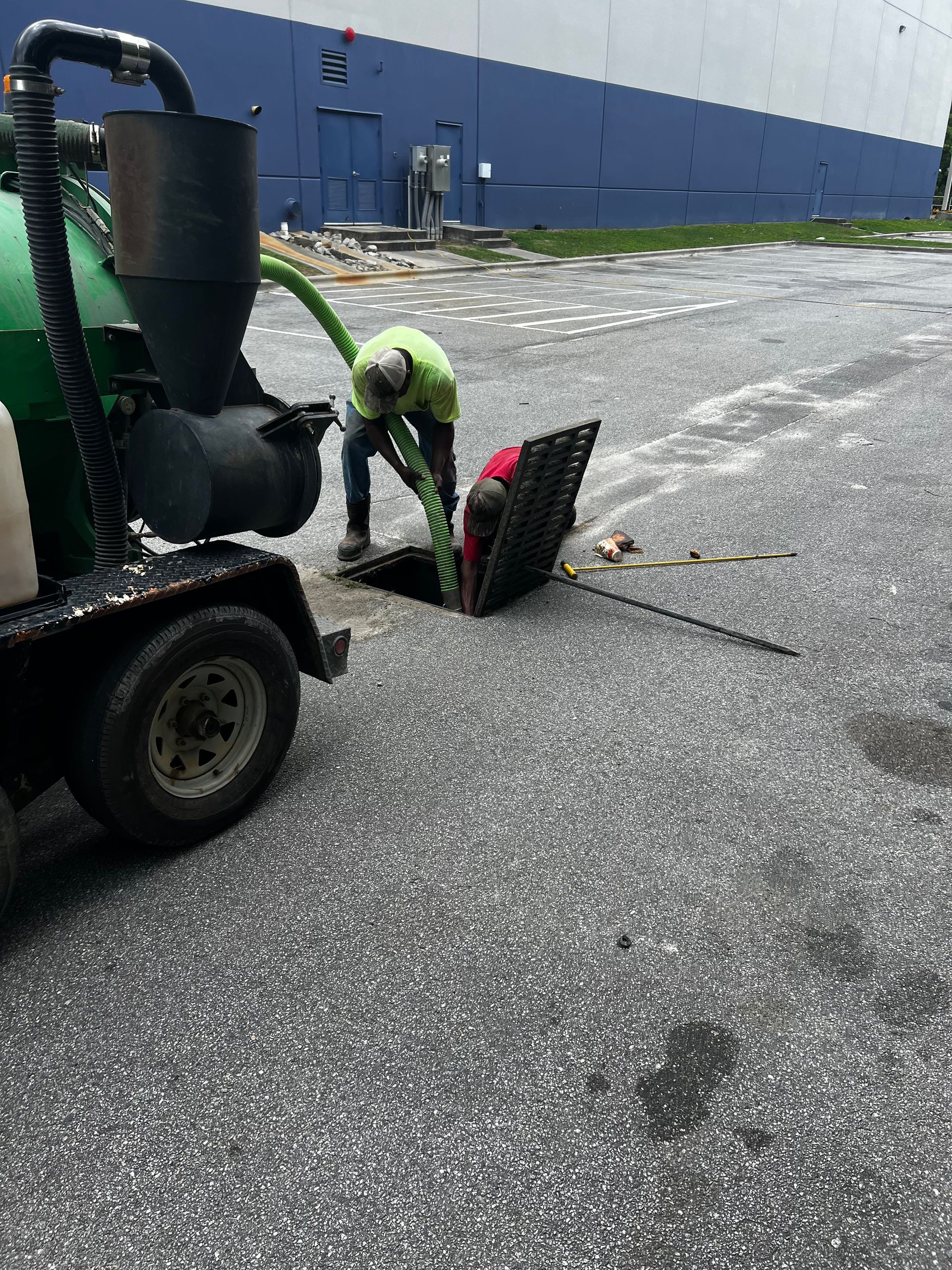 A man is standing in a manhole cover next to a vacuum truck.