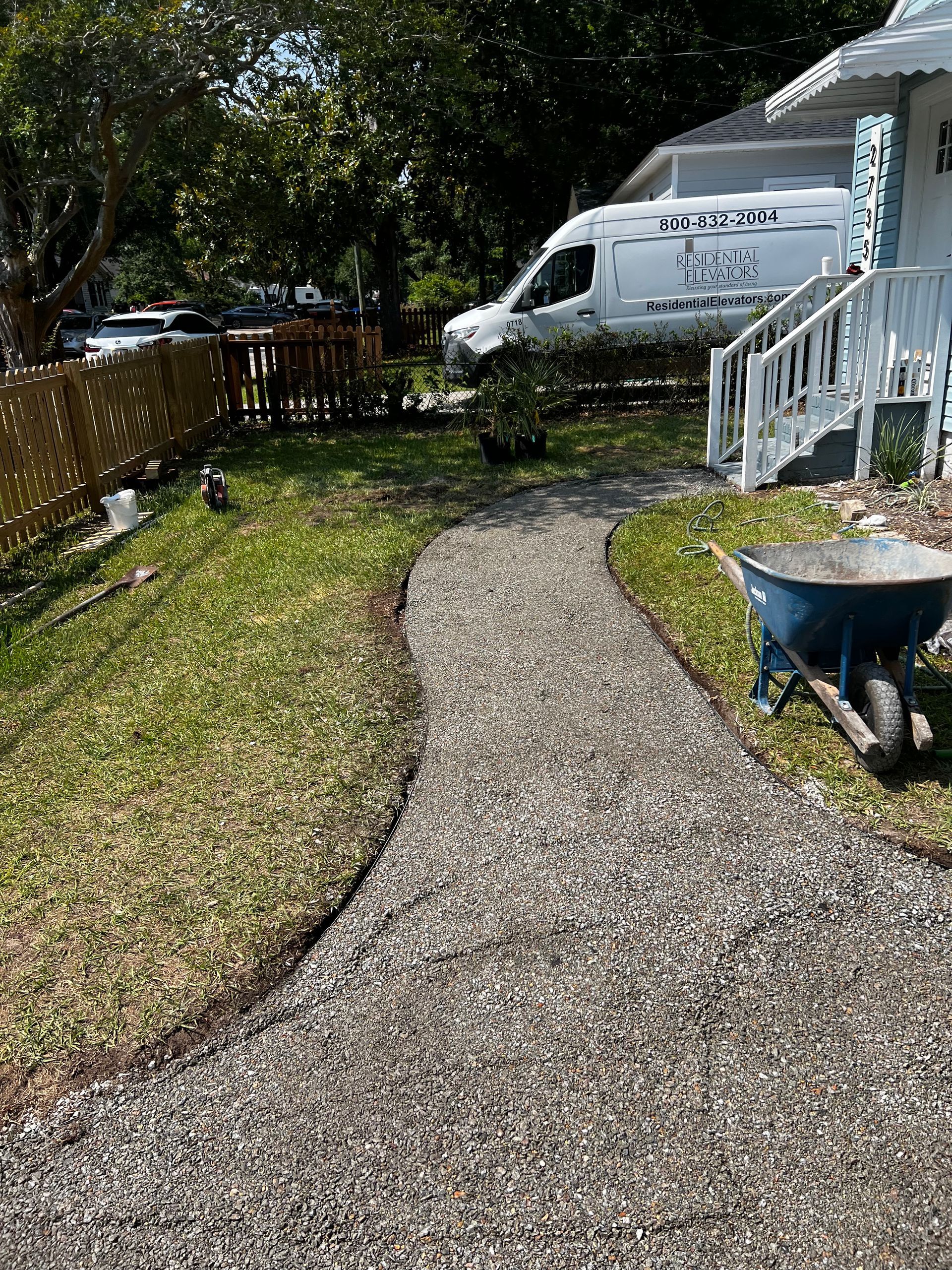 A gravel path leading to a house with a wheelbarrow in front of it.