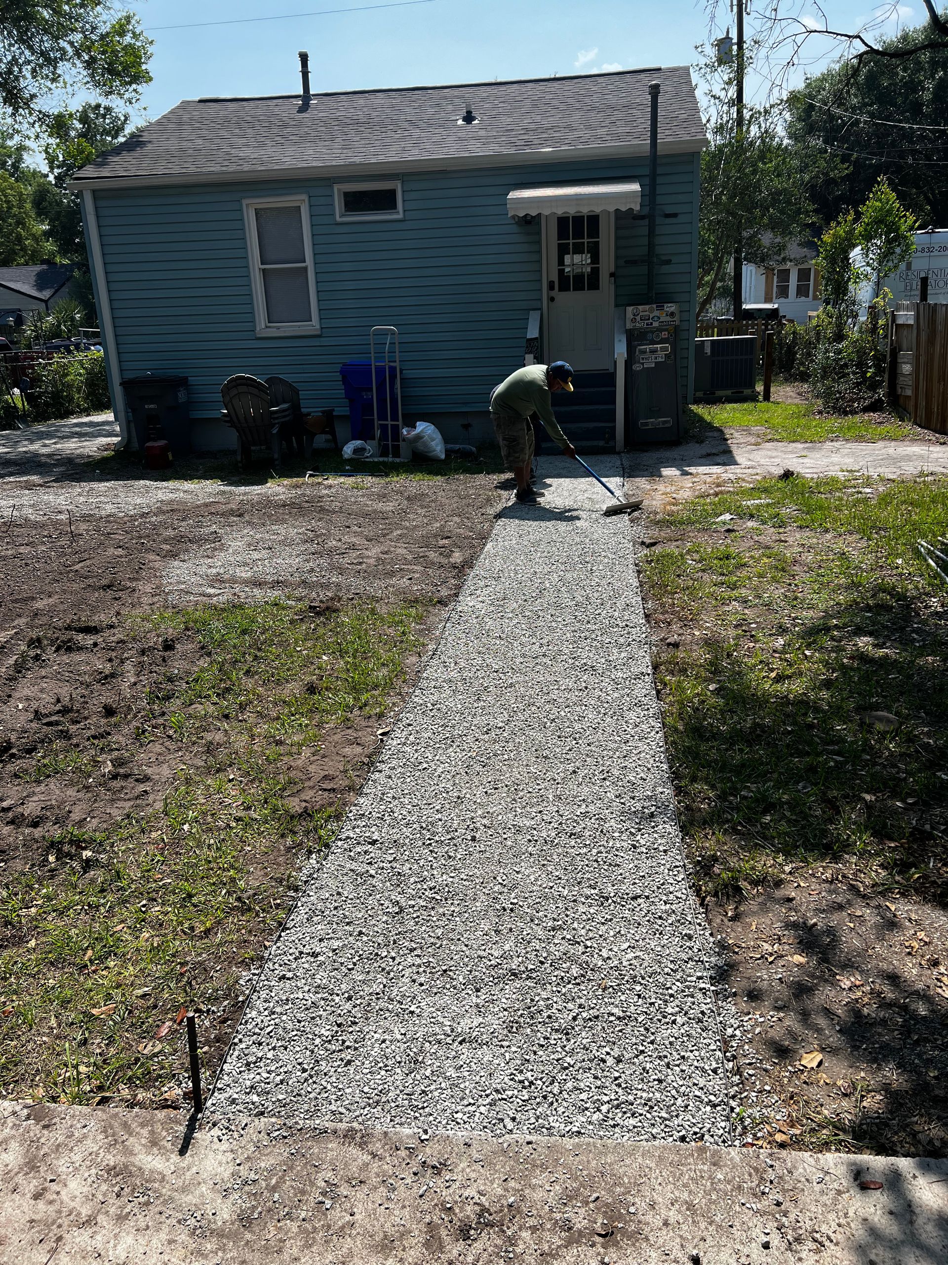 A man is laying gravel on a sidewalk in front of a house.