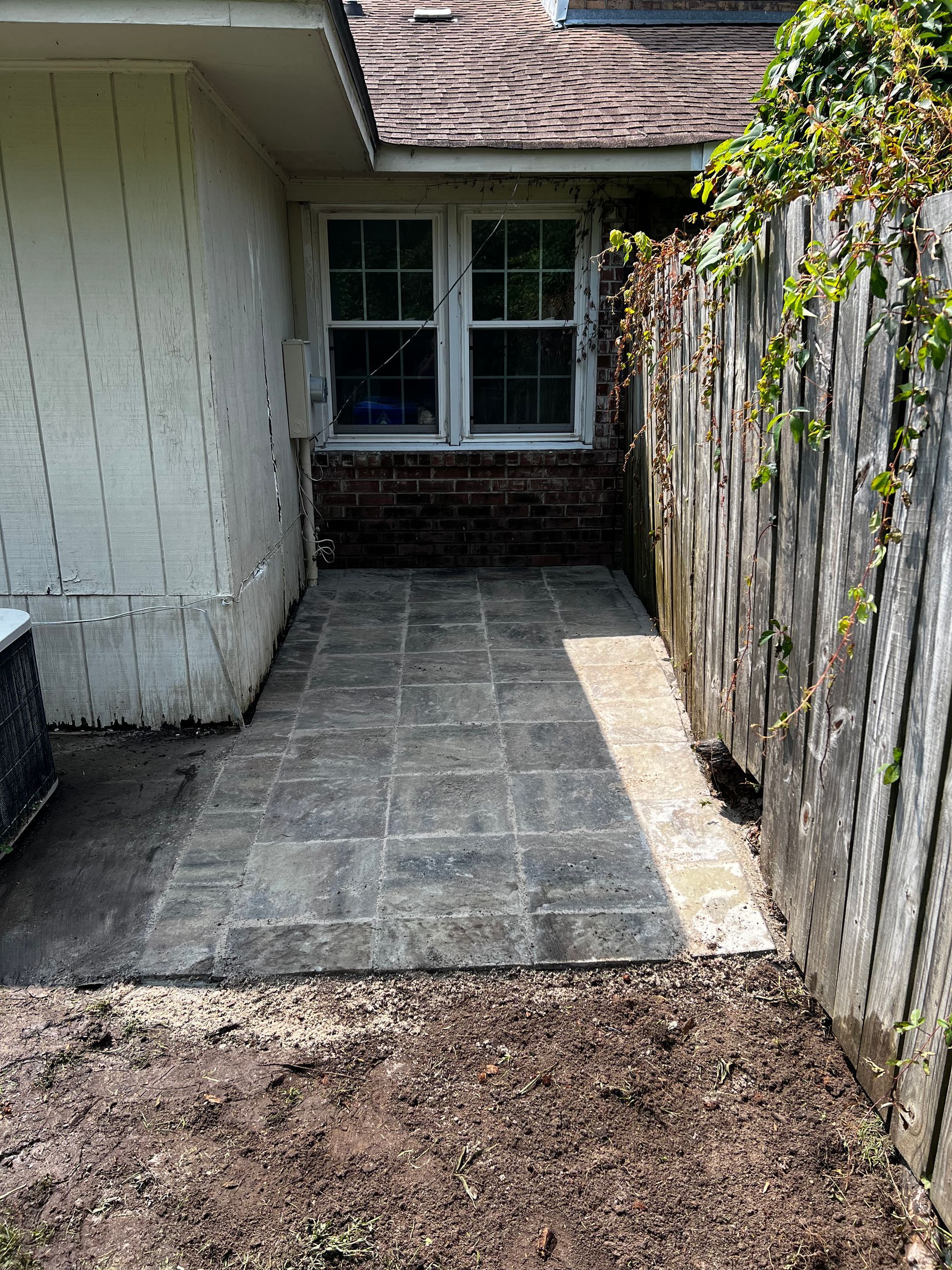 There is a patio in the backyard of a house next to a wooden fence.