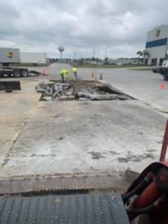 A man in a yellow vest is working on a concrete surface in a parking lot.