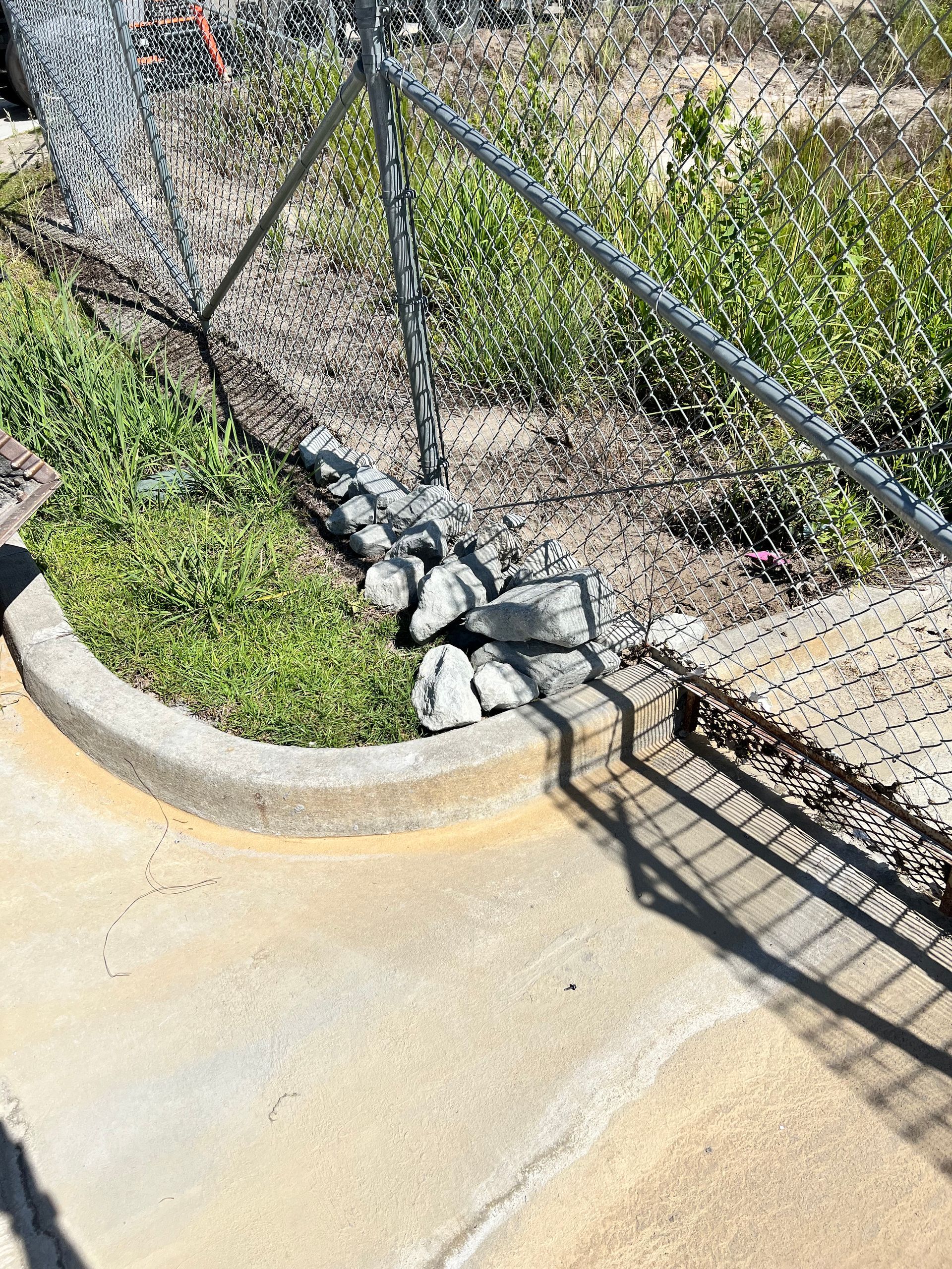 A chain link fence is surrounding a concrete curb.