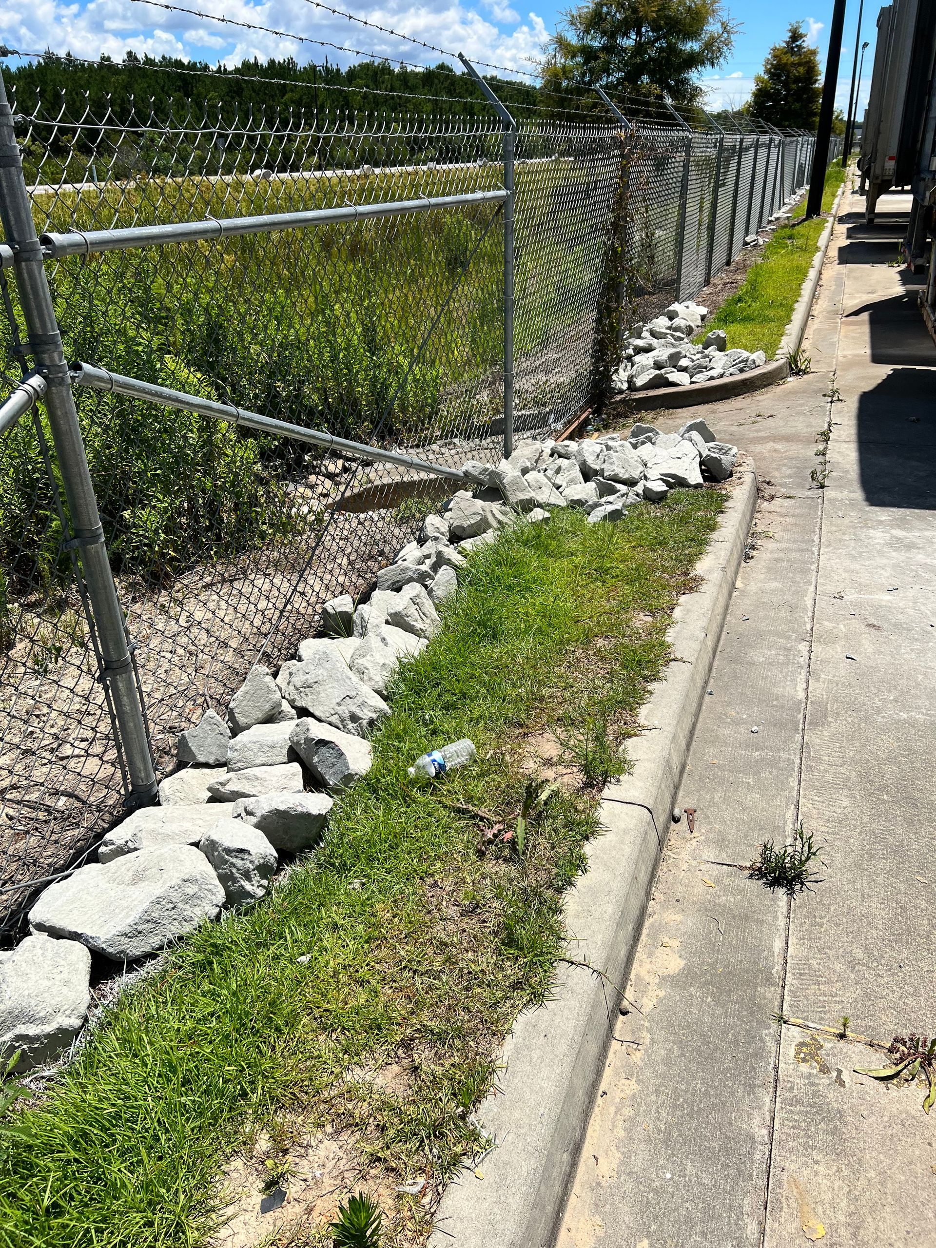 A chain link fence is surrounded by rocks and grass on the side of the road.