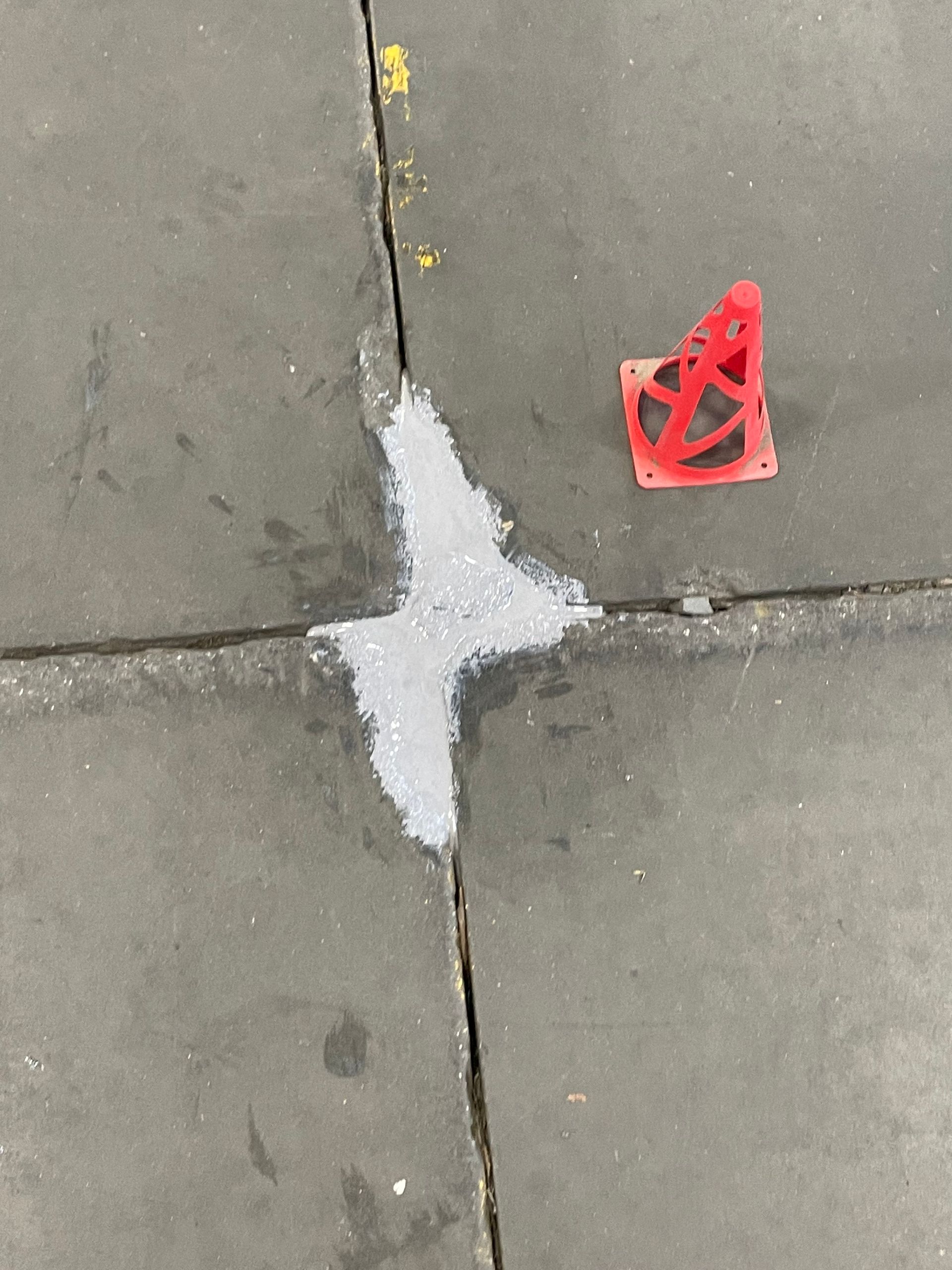 A red cone is on the sidewalk next to a white cross