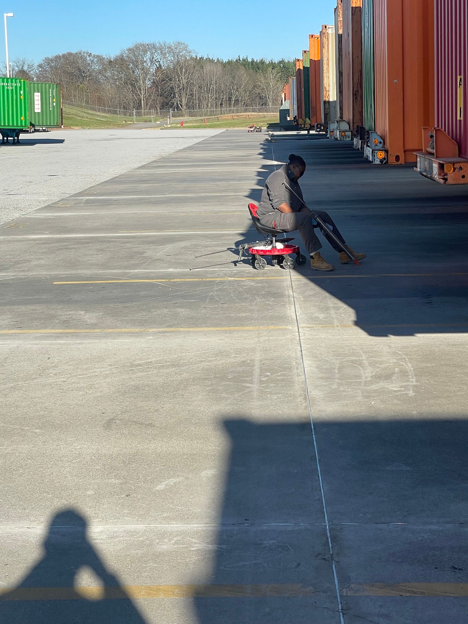 A man sits on a red scooter in a parking lot