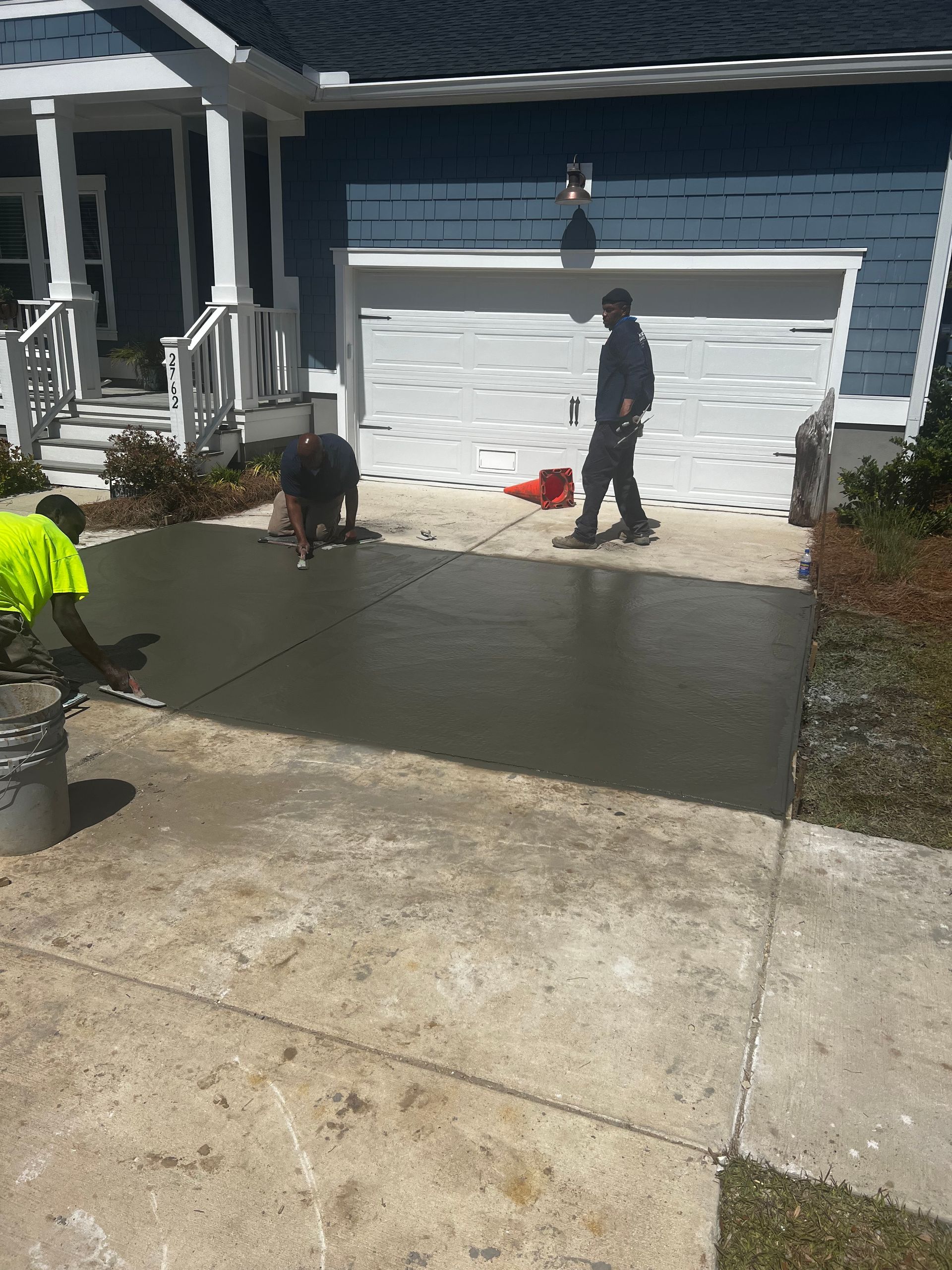 A couple of men are working on a concrete driveway in front of a house.