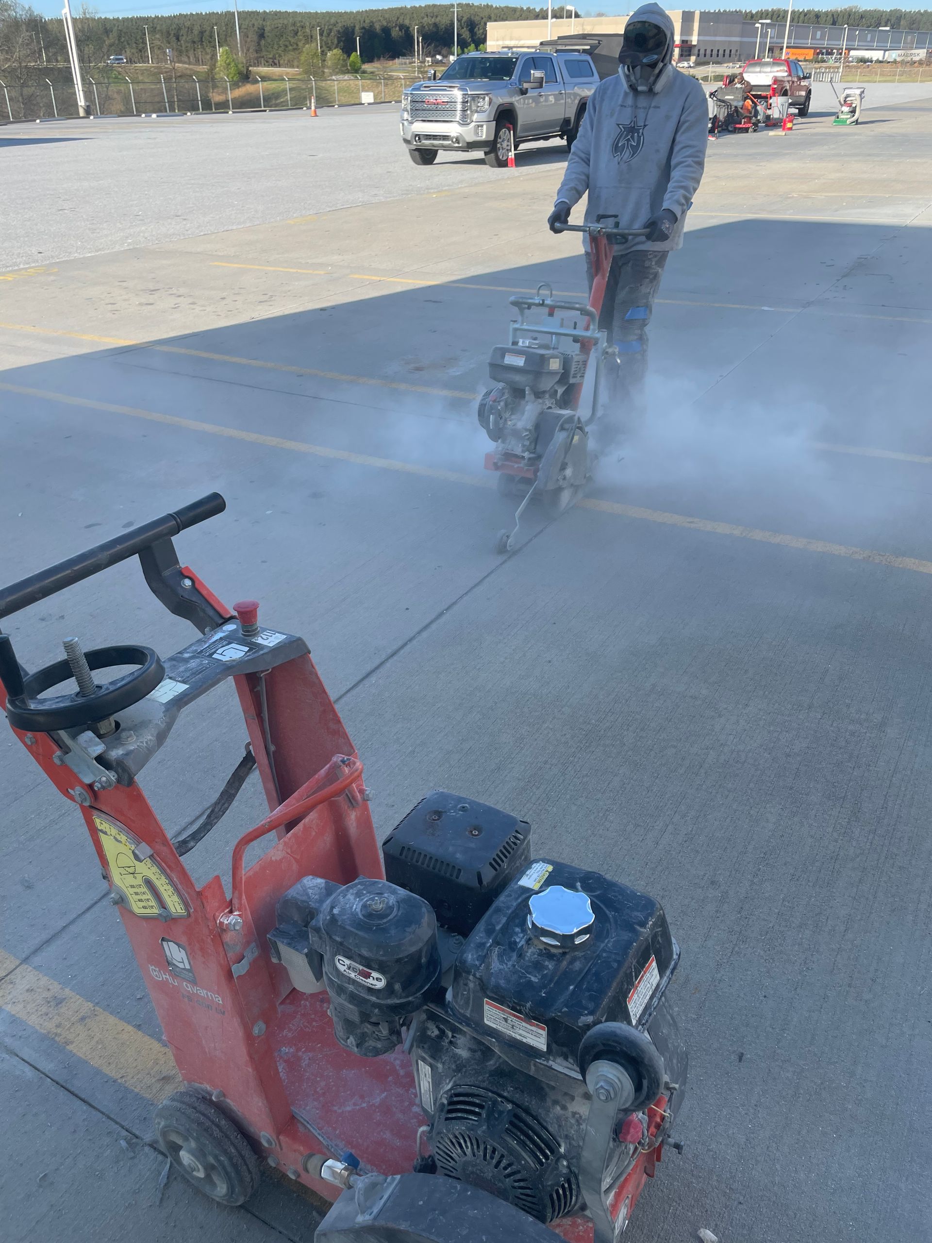 A man is using a machine to cut concrete in a parking lot.