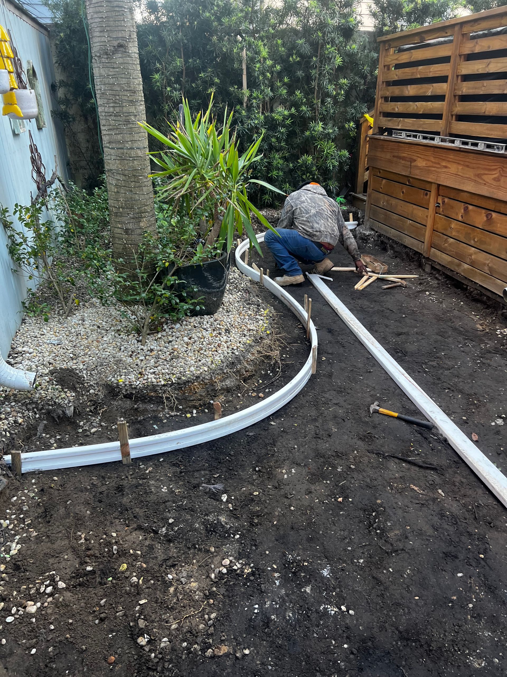 A man is working on a pipe in the dirt in a backyard.