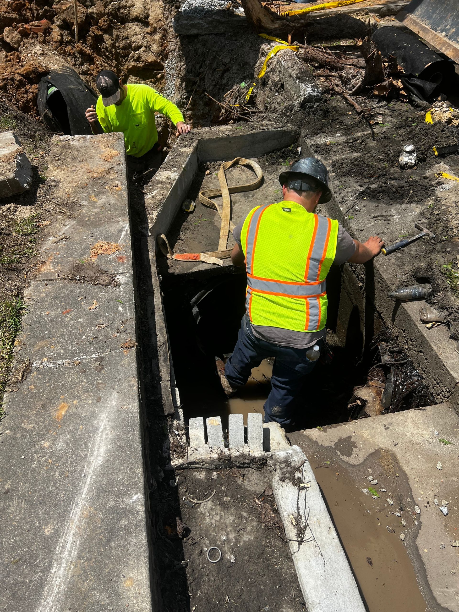 A man in a yellow vest is standing in a hole in the ground.
