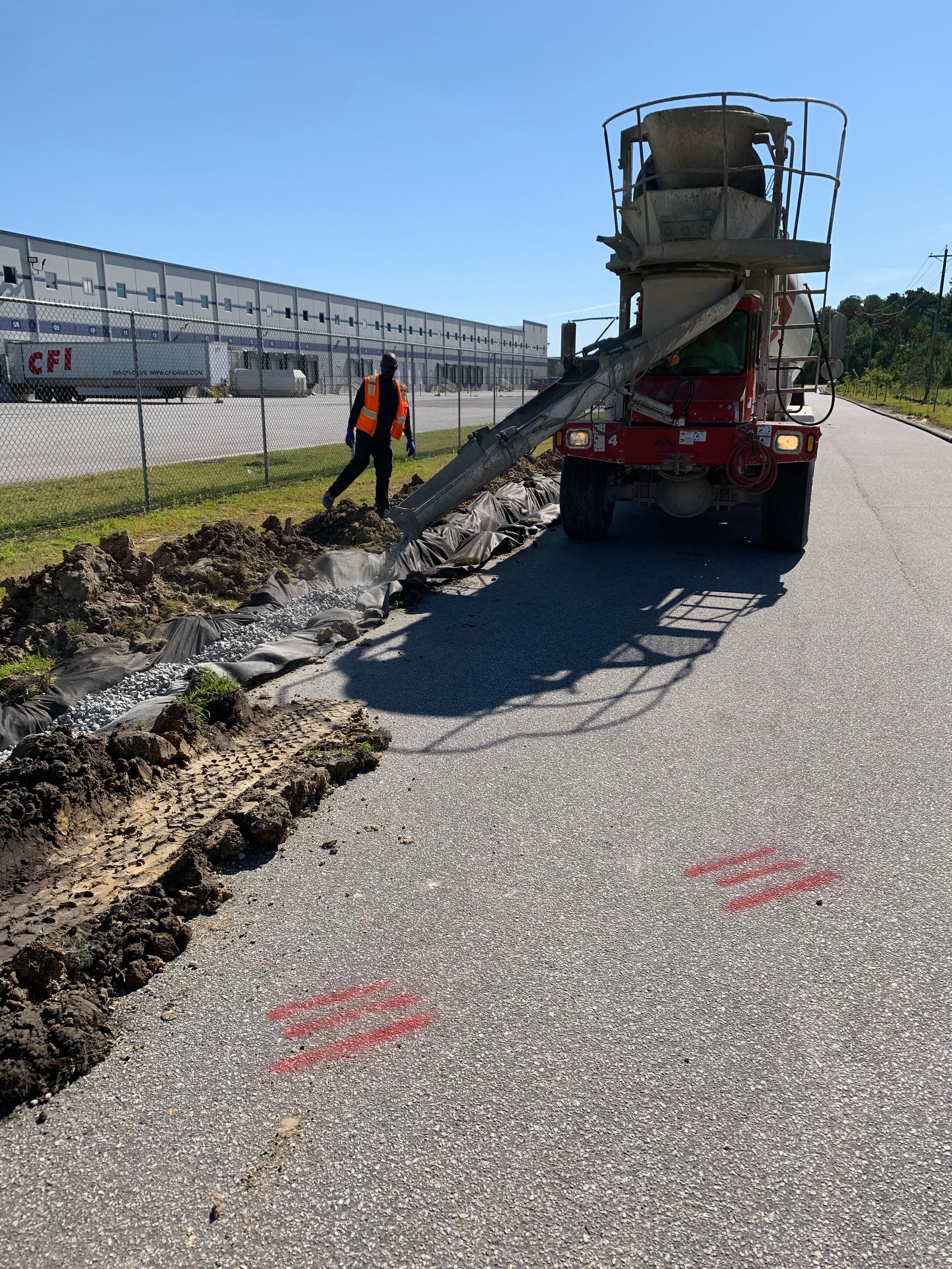 A concrete mixer is pouring concrete on the side of a road.