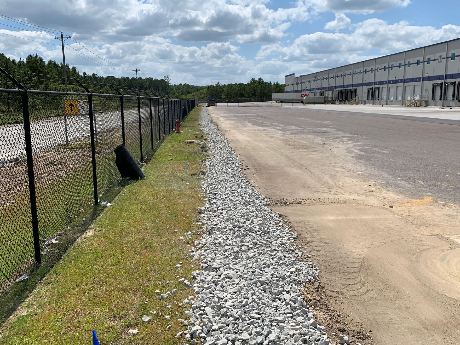 A chain link fence surrounds a gravel road in front of a large building.