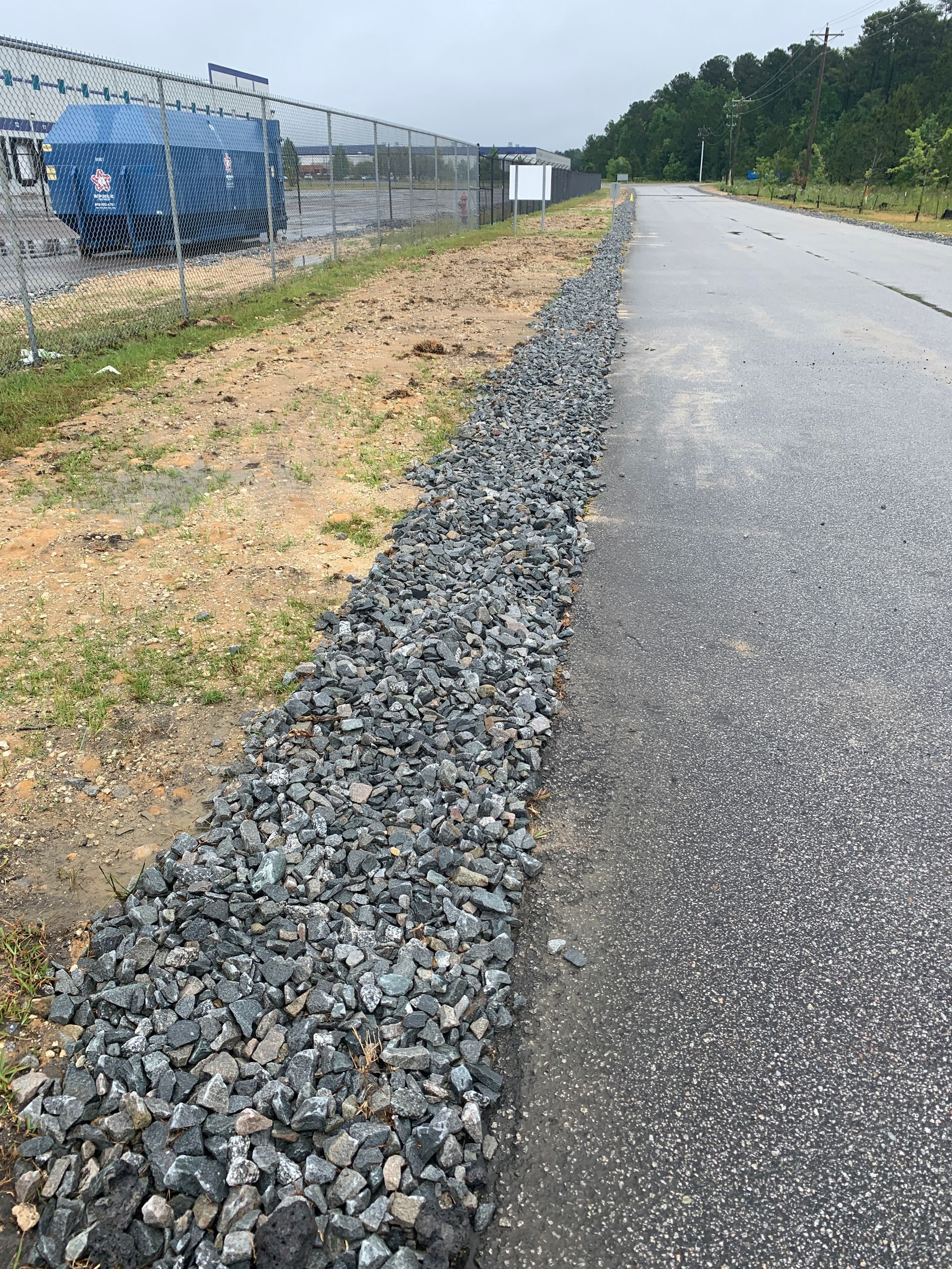 A road with gravel on the side of it and a fence in the background.