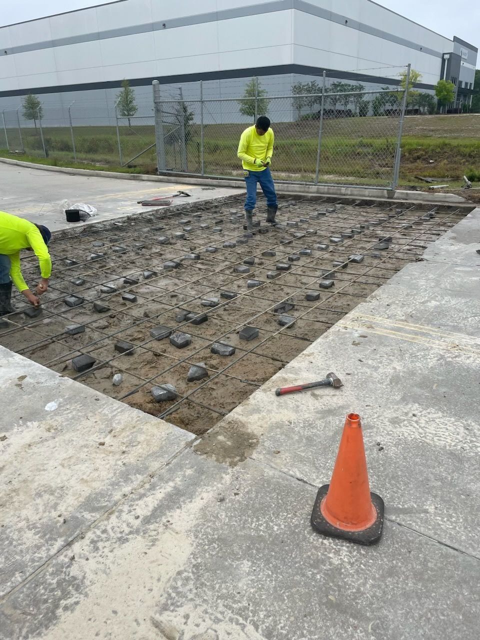 Two men are working on a concrete driveway in front of a large building
