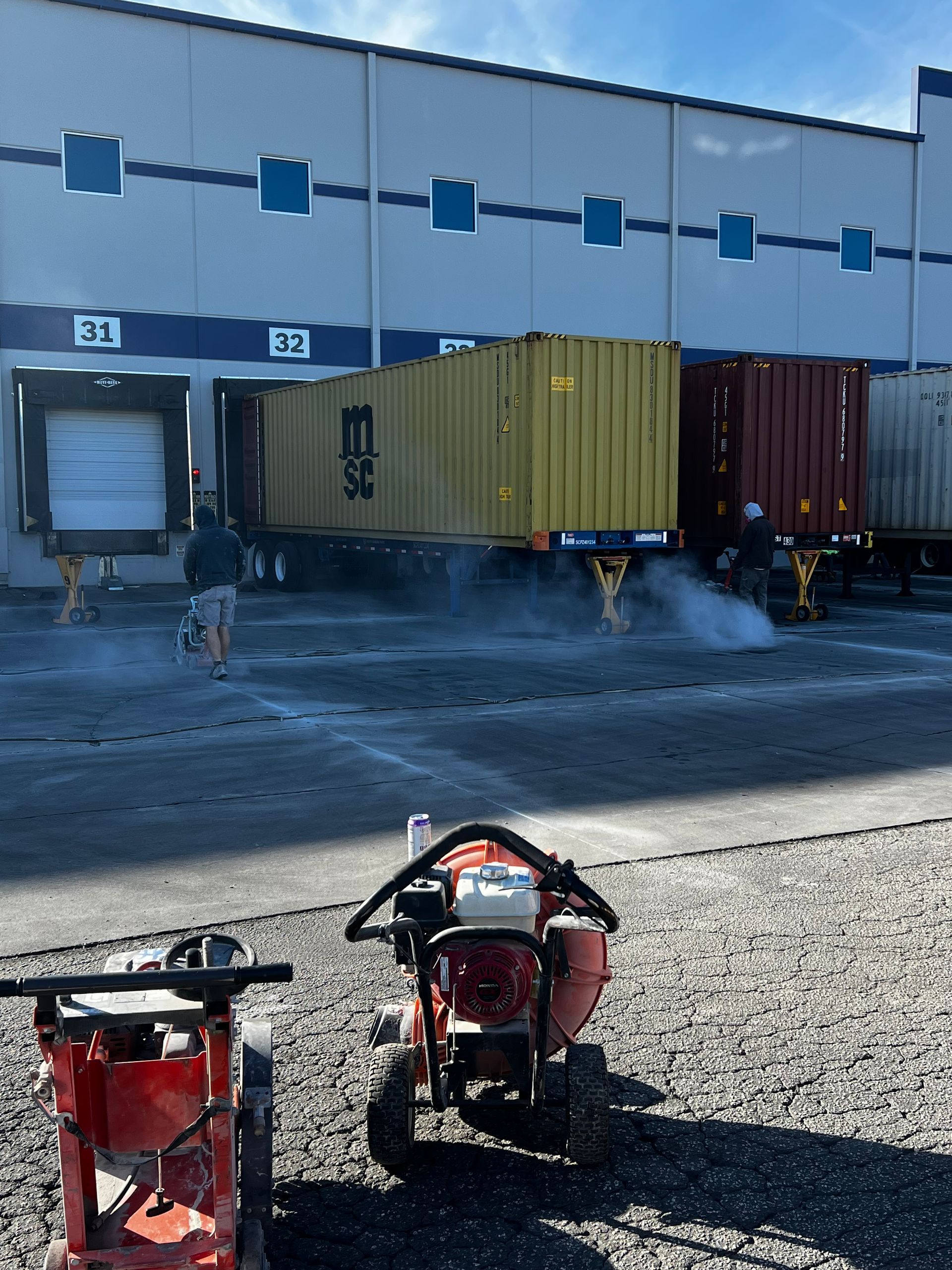 A tractor is parked in front of a warehouse with a large yellow container in the background.