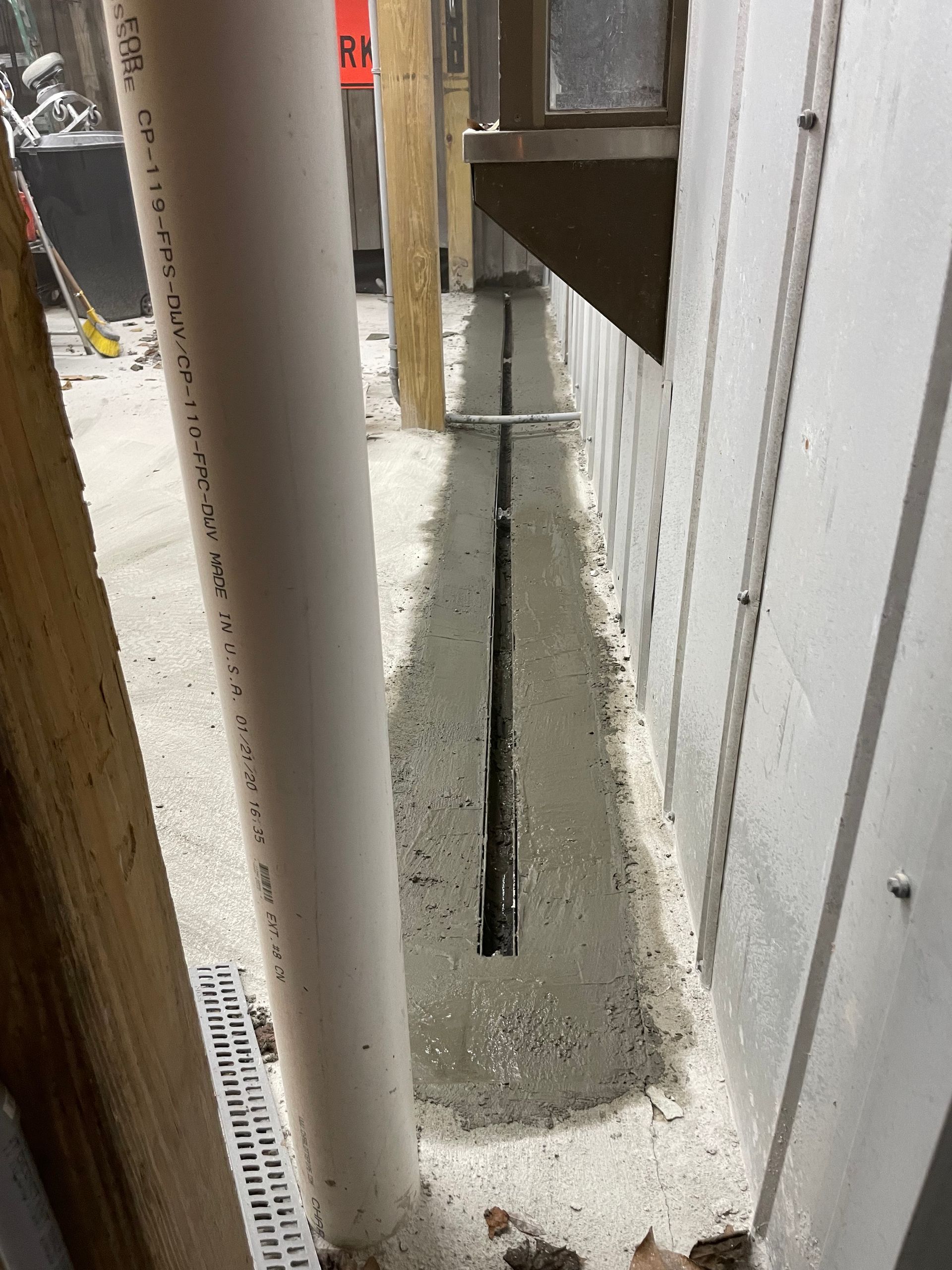 A drain pipe is being installed in a basement next to a wall.