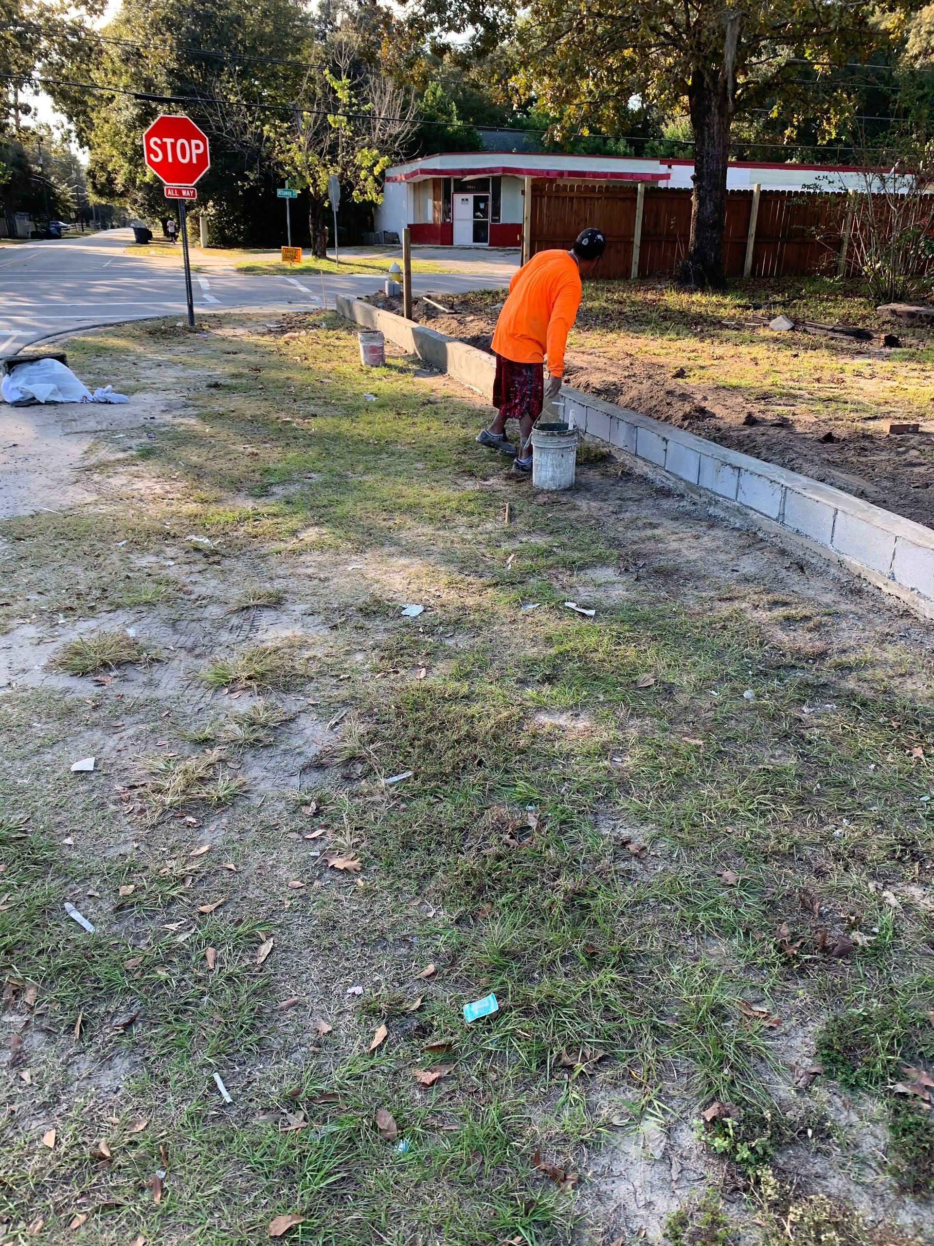 A man is working on a sidewalk in front of a stop sign.
