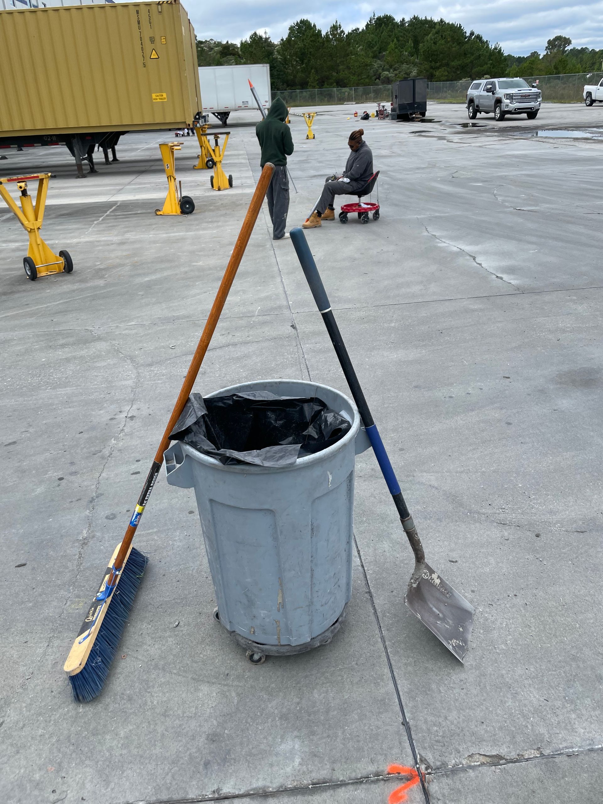A trash can with a broom and shovel in it