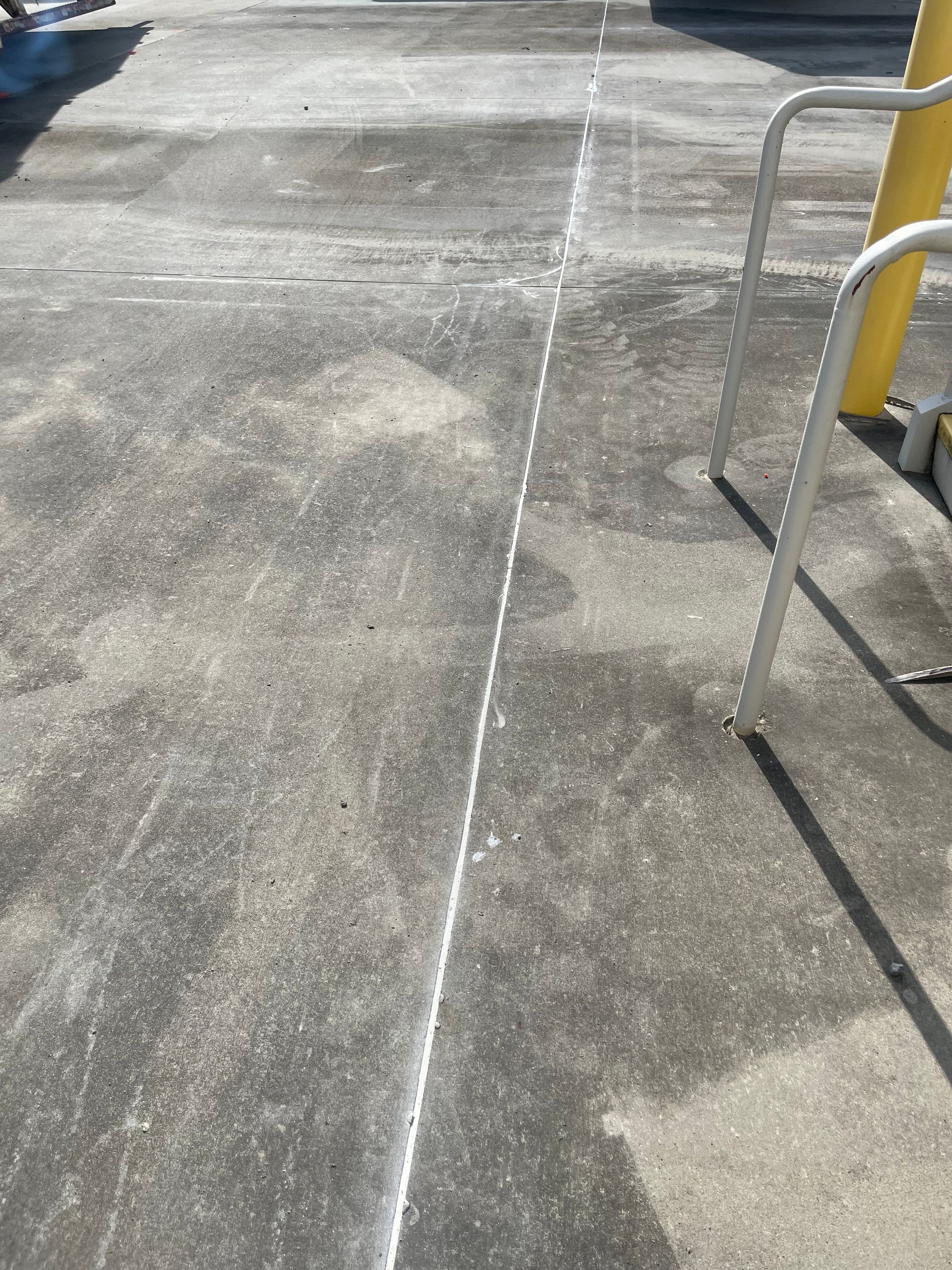 A concrete sidewalk with a yellow pole in the background.