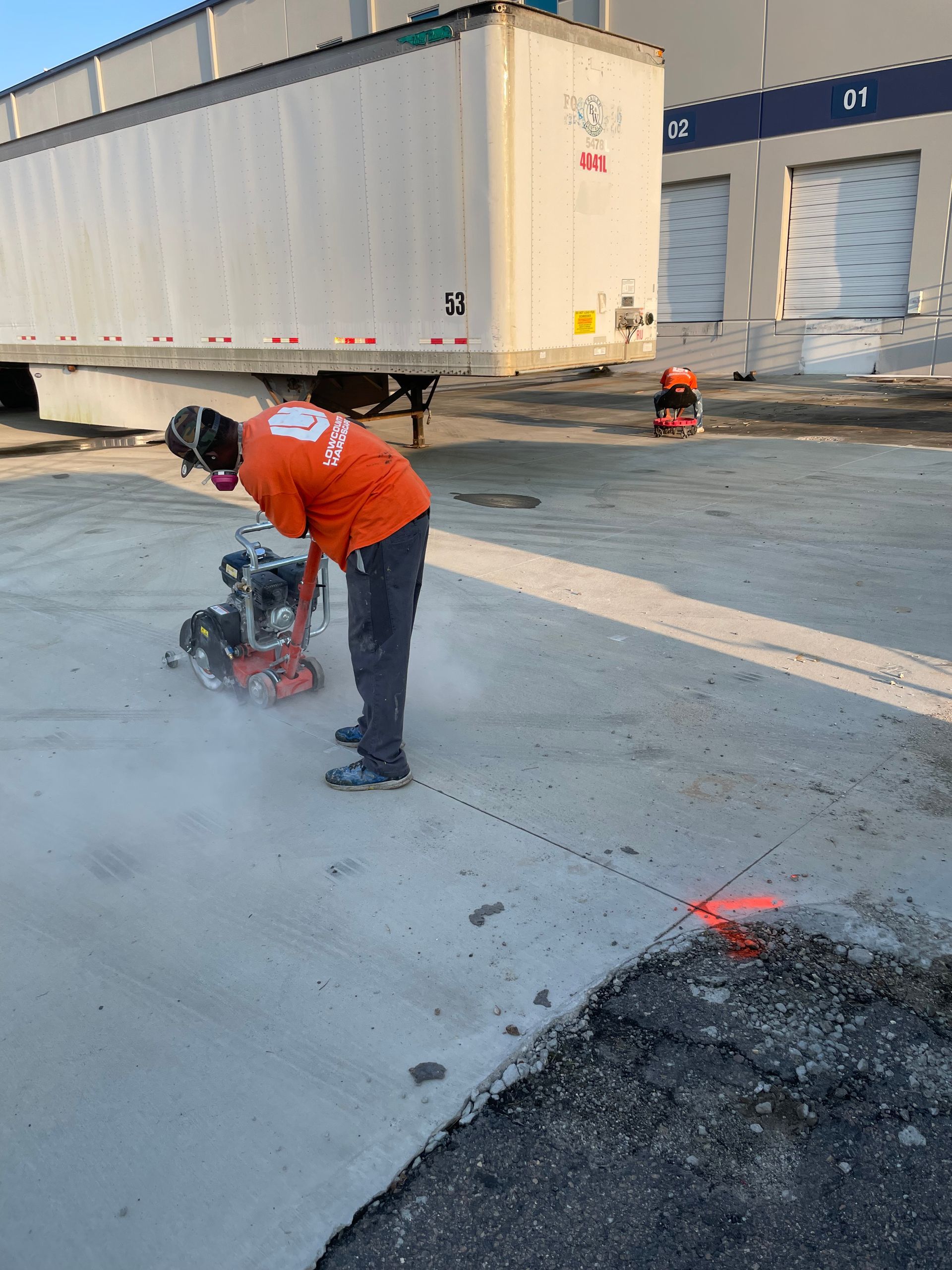 A man is cutting a hole in the ground in a parking lot.