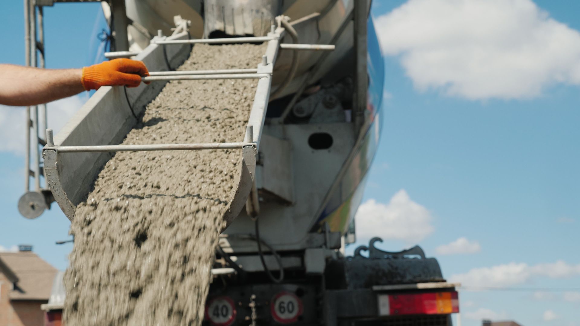 Ready-mix concrete supplier worker pours foundation, guiding chute on gravel construction site.