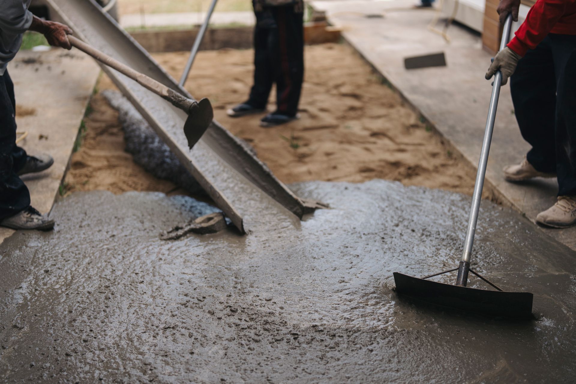 Workers spread wet concrete poured from chute by a ready-mix concrete supplier at job site.