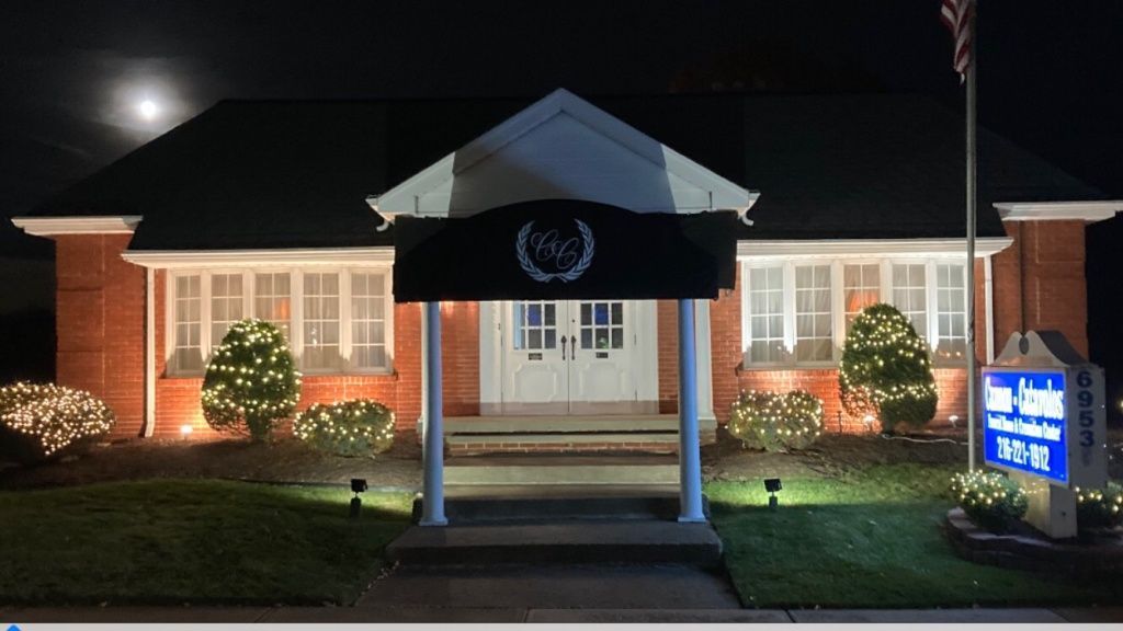 Brick building with illuminated sign, Christmas lights, and American flag at night.