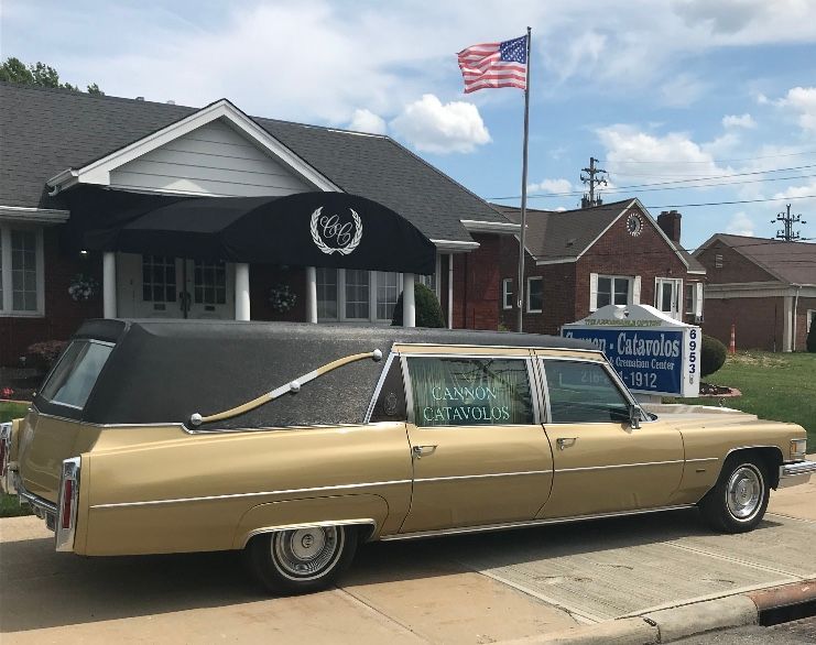 Gold hearse parked outside a funeral home with an American flag.
