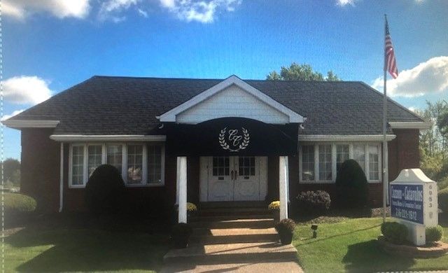 Brick building with black roof; US flag and sign on the lawn.