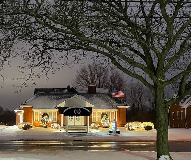Snow-covered building with Christmas lights, American flag, and tree in foreground.