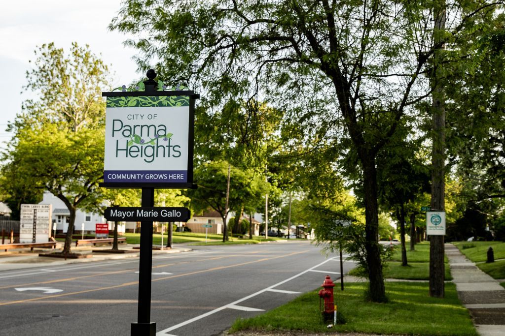 Sign for Parma Heights, Ohio, with street scene; trees, road, and other signs visible.