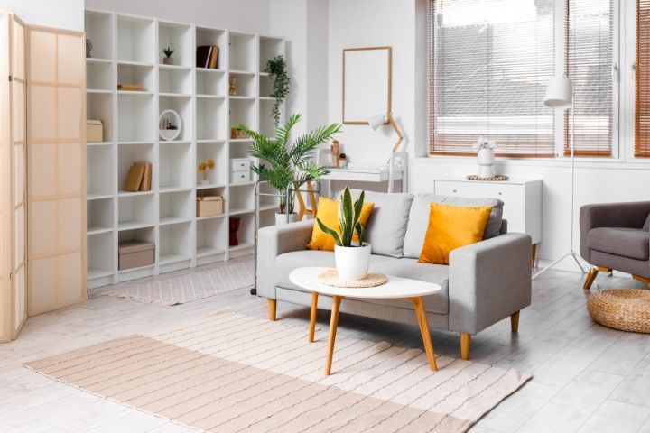 Living room with gray sofa, yellow pillows, white shelving, and natural light.