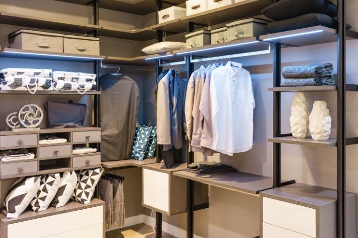 Modern walk-in closet with gray shelves, drawers, and hanging clothes, with LED lighting.