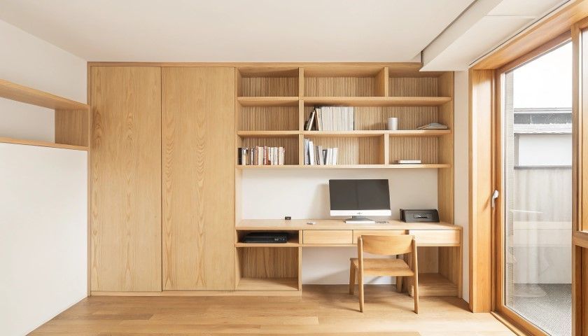 Wooden built-in desk with shelves and cabinets, and a window in a light-filled room.