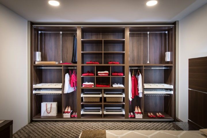 Built-in dark wood closet with shelves, hanging rods, and pull-out drawers; red and white clothing displayed.
